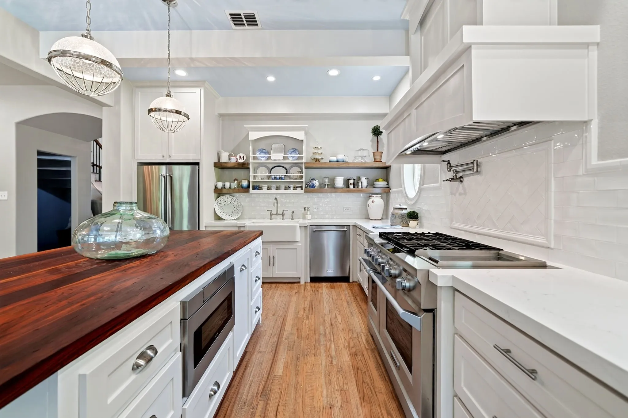Gourmet kitchen featuring a substantial wood-finish island with integrated microwave, professional-grade stainless steel appliances, a pot filler, and open shelving