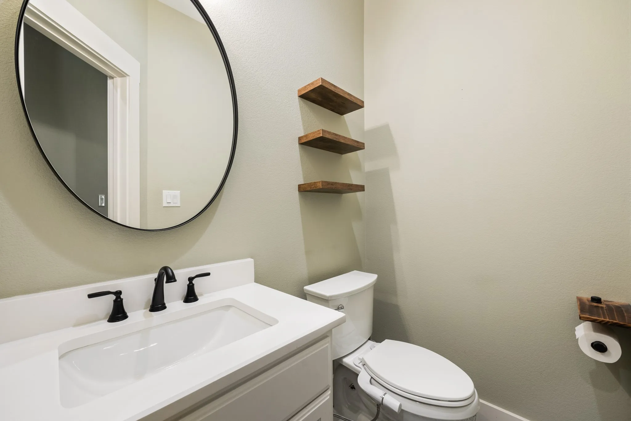 White vanity with integrated sink, black faucet, and round wall-mounted mirror