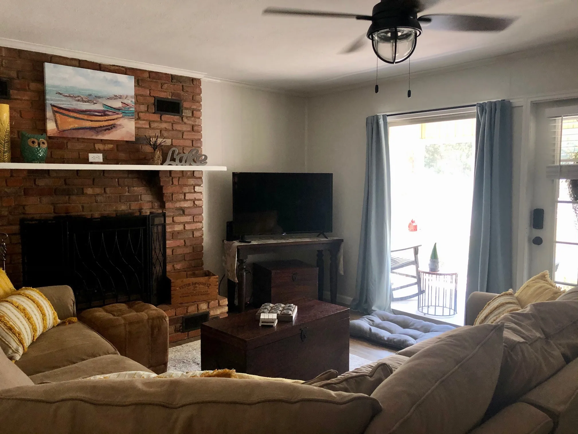 Exposed brick fireplace with a white mantel, ceiling fan with light fixture, light wood-finish flooring, and a sliding glass door