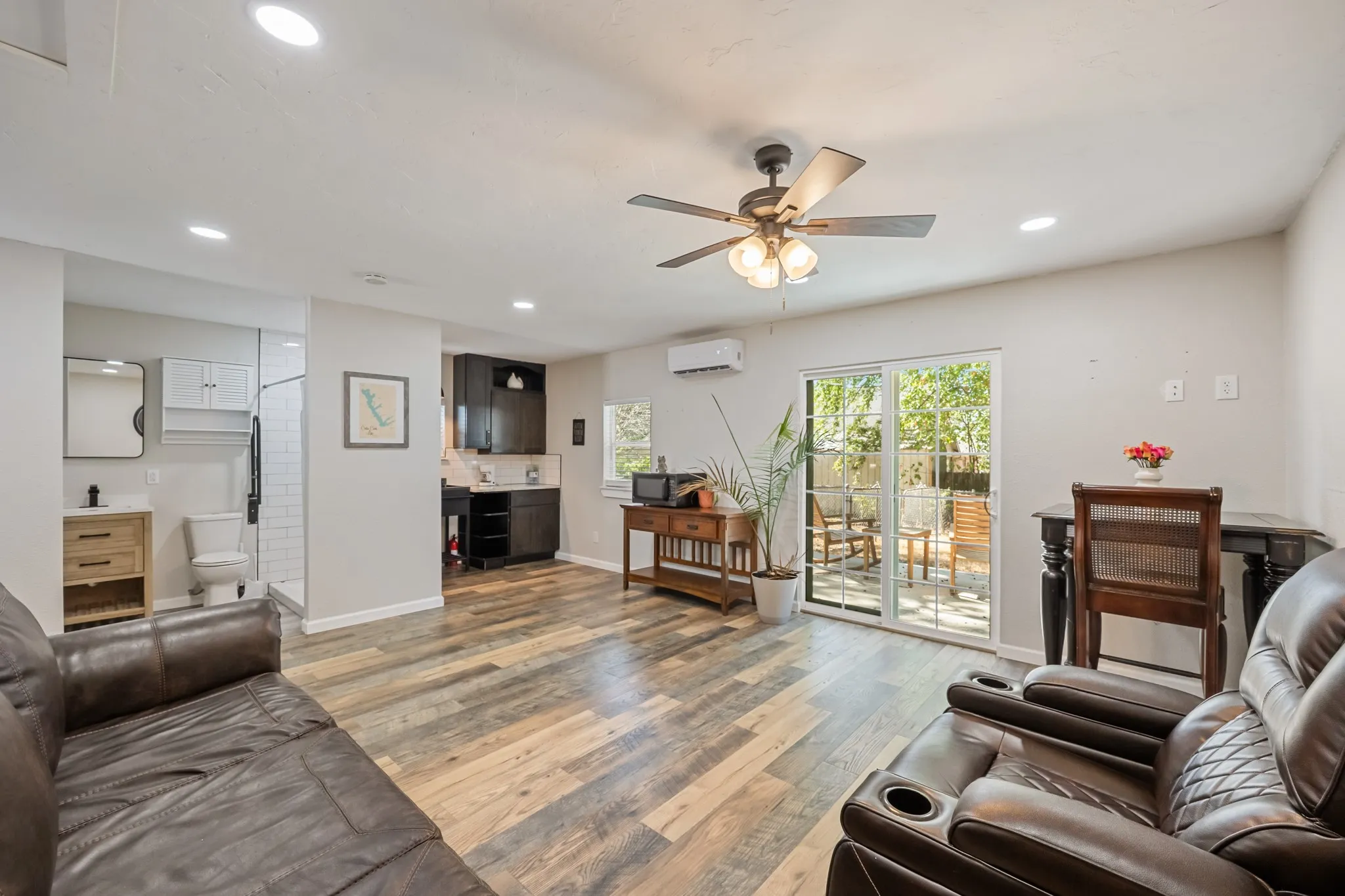 Recessed lighting, wood-finish flooring, a ceiling fan, a kitchen area with dark cabinetry, and sliding glass doors to the exterior
