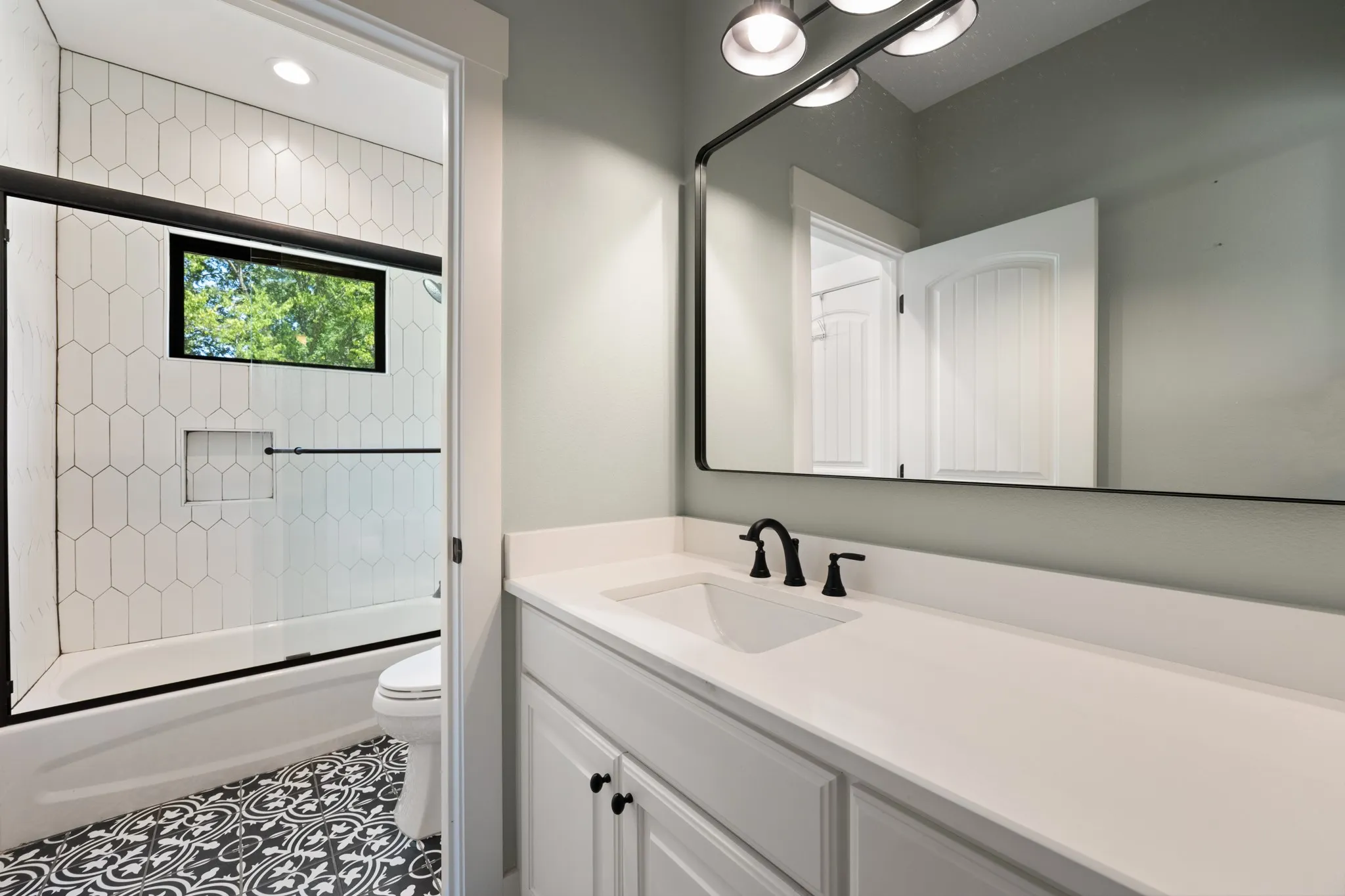 White single vanity with integrated sink and matte black faucet, oversized rectangular mirror, and three-light vanity fixture