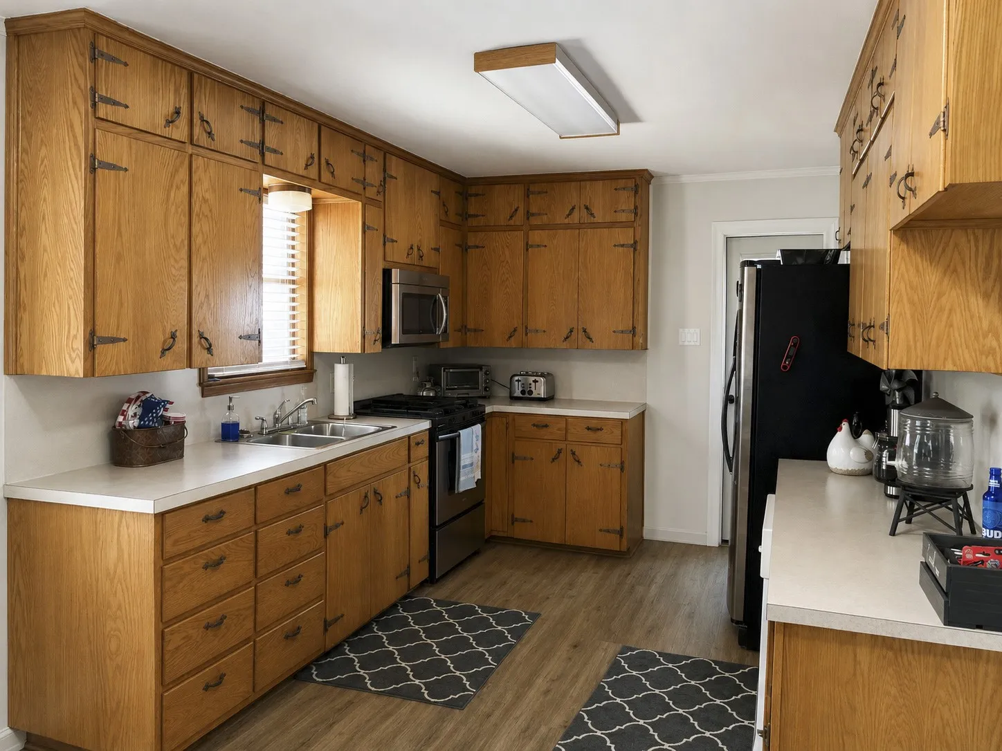 Guest Galley-style kitchen featuring wood cabinetry, white countertops, a stainless steel double basin sink, and wood-finish flooring