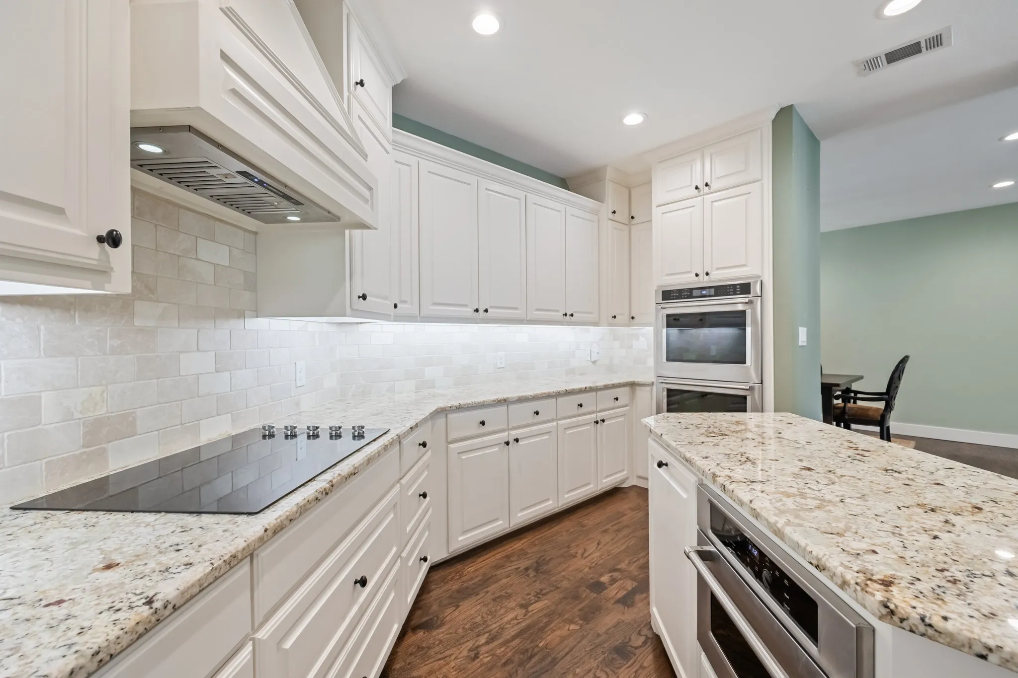 Kitchen featuring white cabinetry, light-toned countertops, a built-in cooktop, and double wall ovens