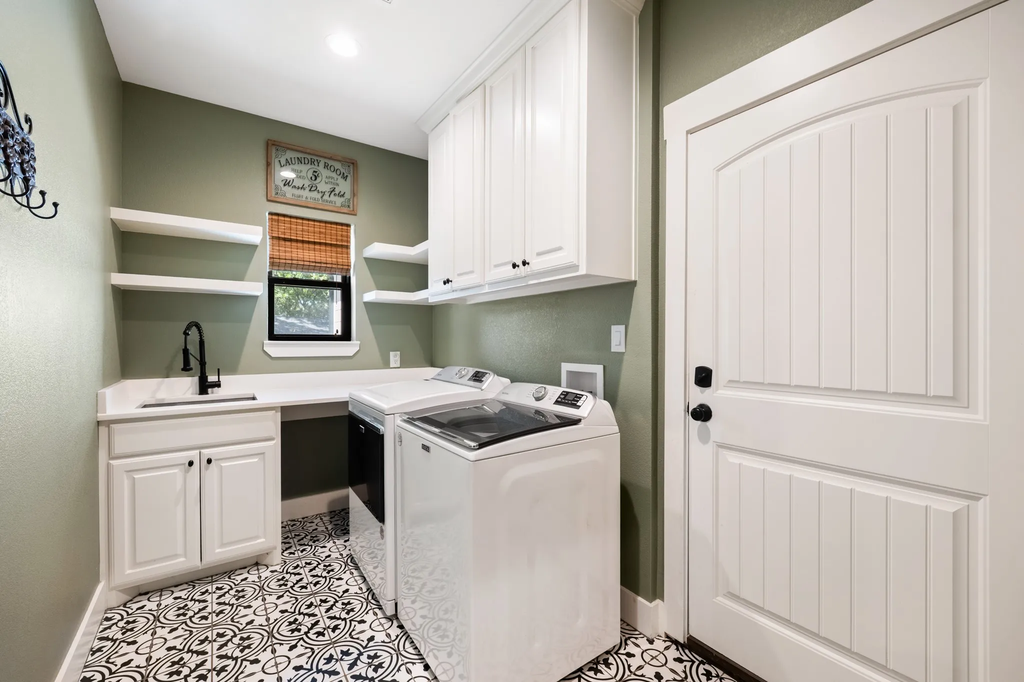 Built-in cabinetry, white countertop, integrated sink with matte black faucet, open shelving, and patterned floor tile