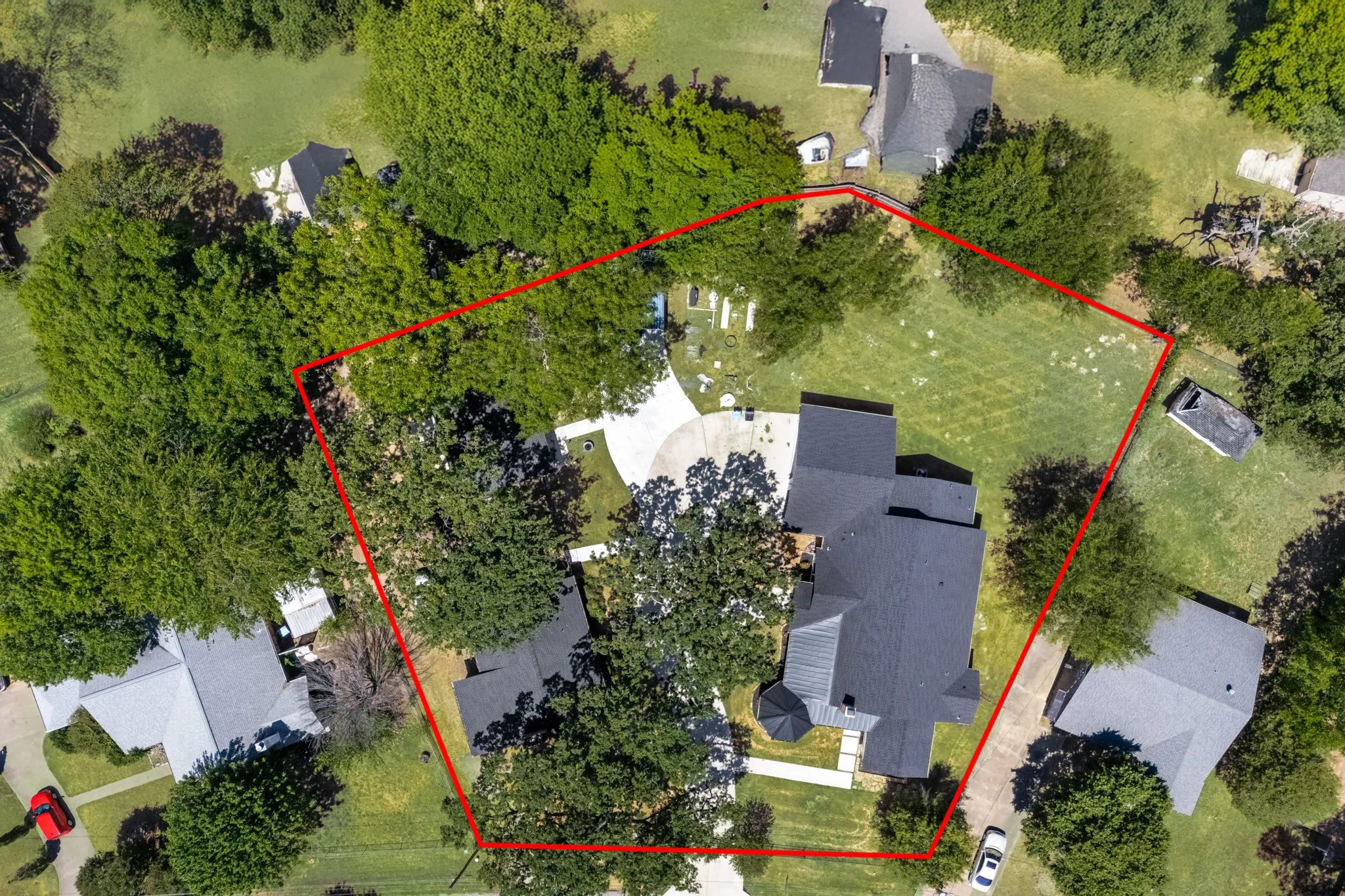 Aerial perspective showcasing a large residential property with mature trees, expansive green space, and a multi-level home with a dark-pitched roof