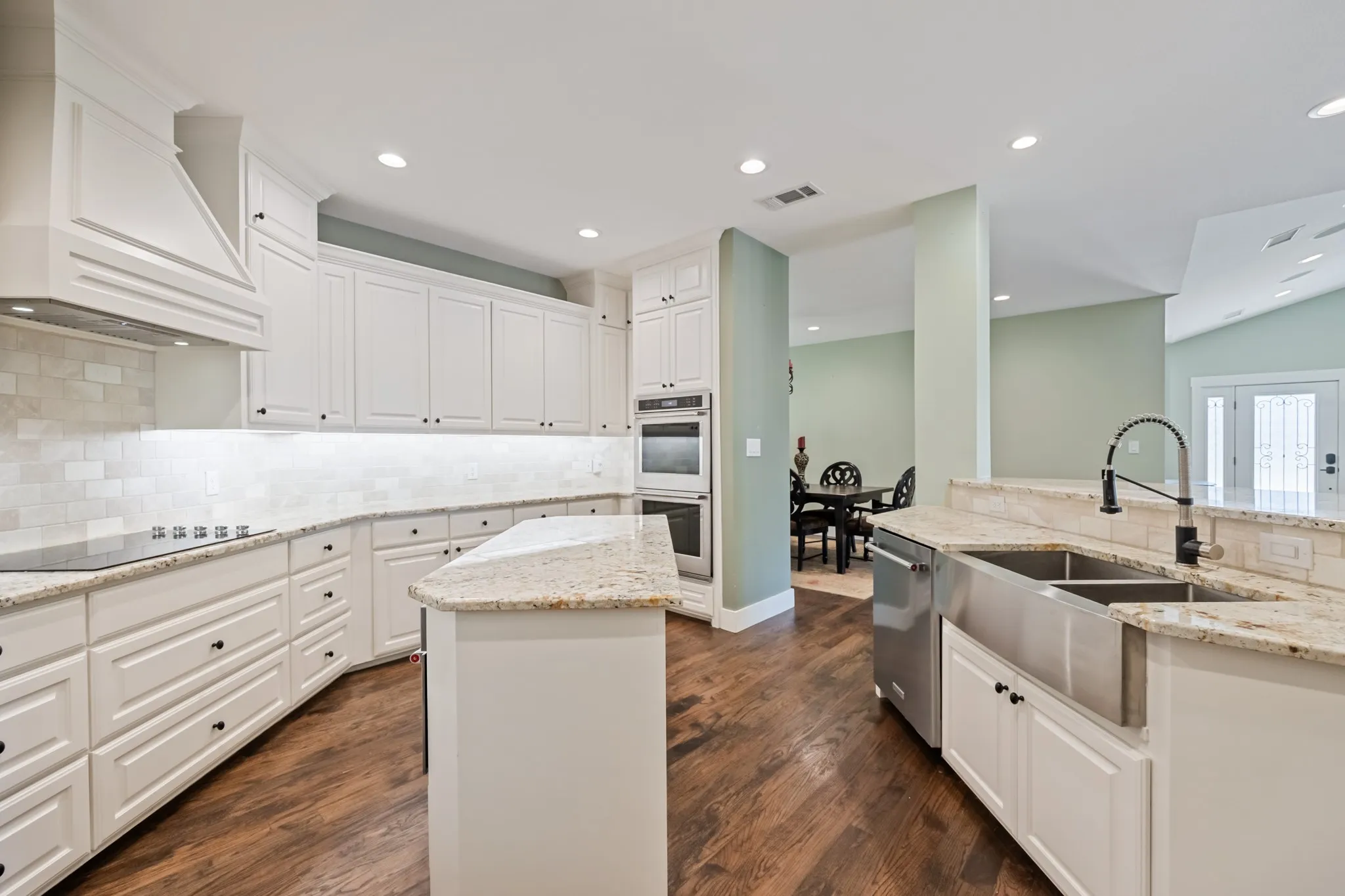 White cabinetry, wood-finish flooring, stainless steel appliances, light-toned countertops, and mosaic tile backsplash