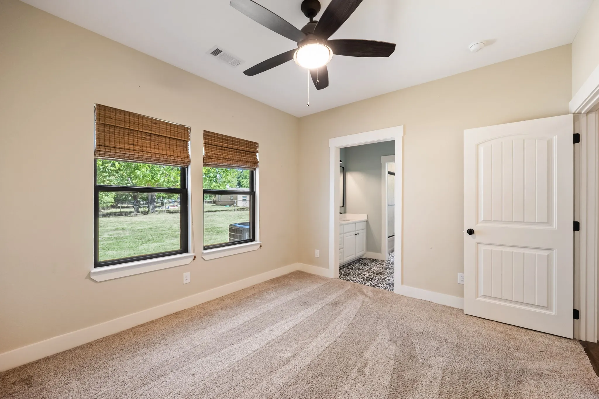 Vaulted ceiling with a ceiling fan, two windows with woven shades, carpeted flooring, and a paneled door