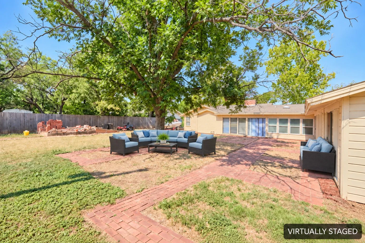 Expansive backyard featuring a red brick patio, mature trees, and a wooden perimeter fence