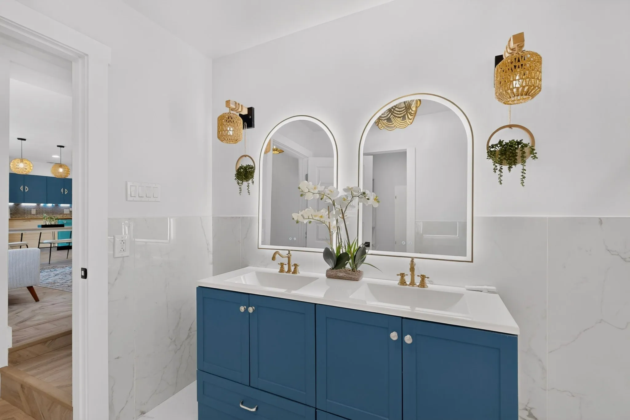 Dual arched illuminated mirrors over a blue vanity with double undermount sinks and gold-finish fixtures