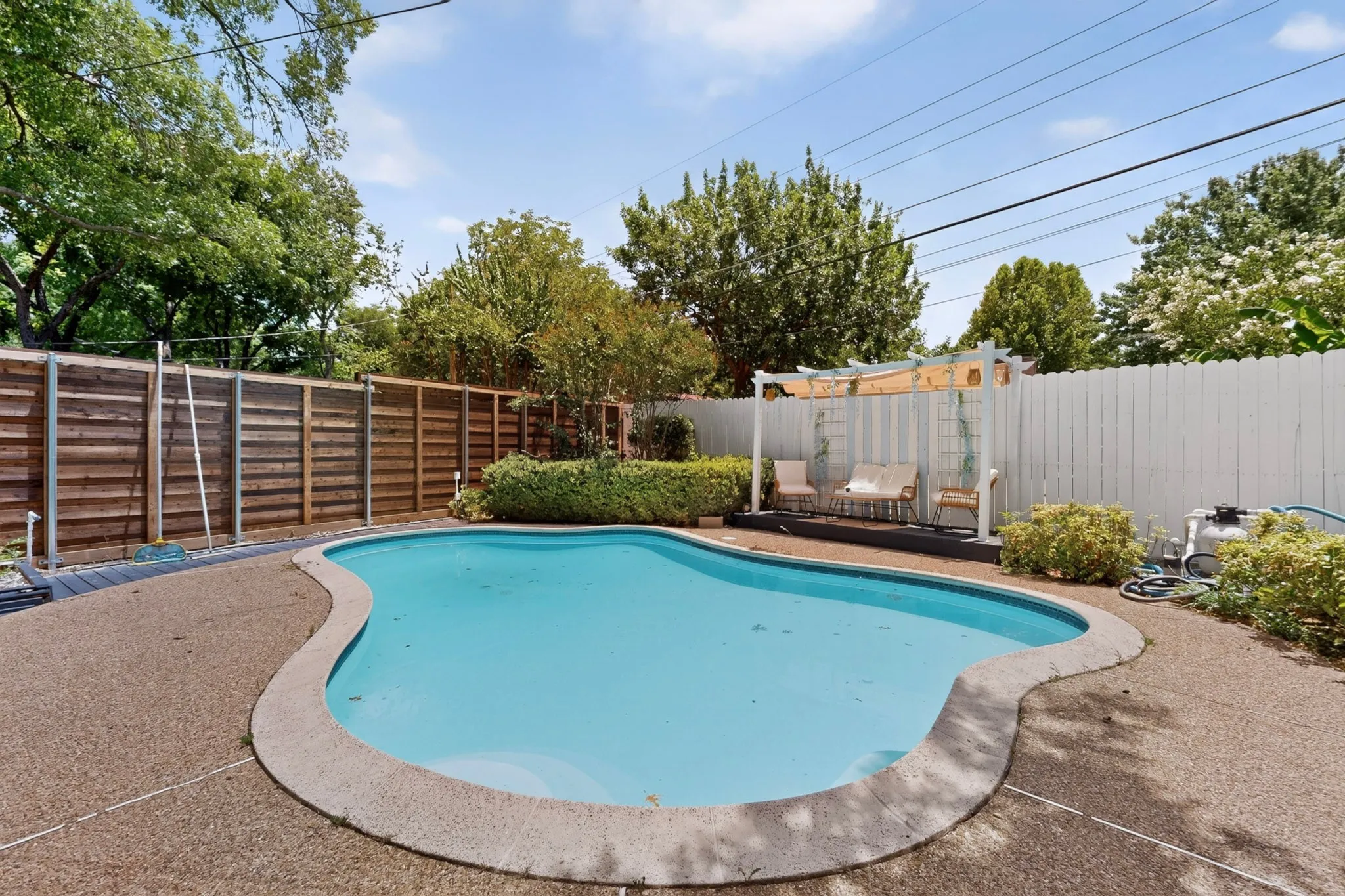 Freeform swimming pool with exposed aggregate concrete decking, wood privacy fencing, and an integrated pergola structure