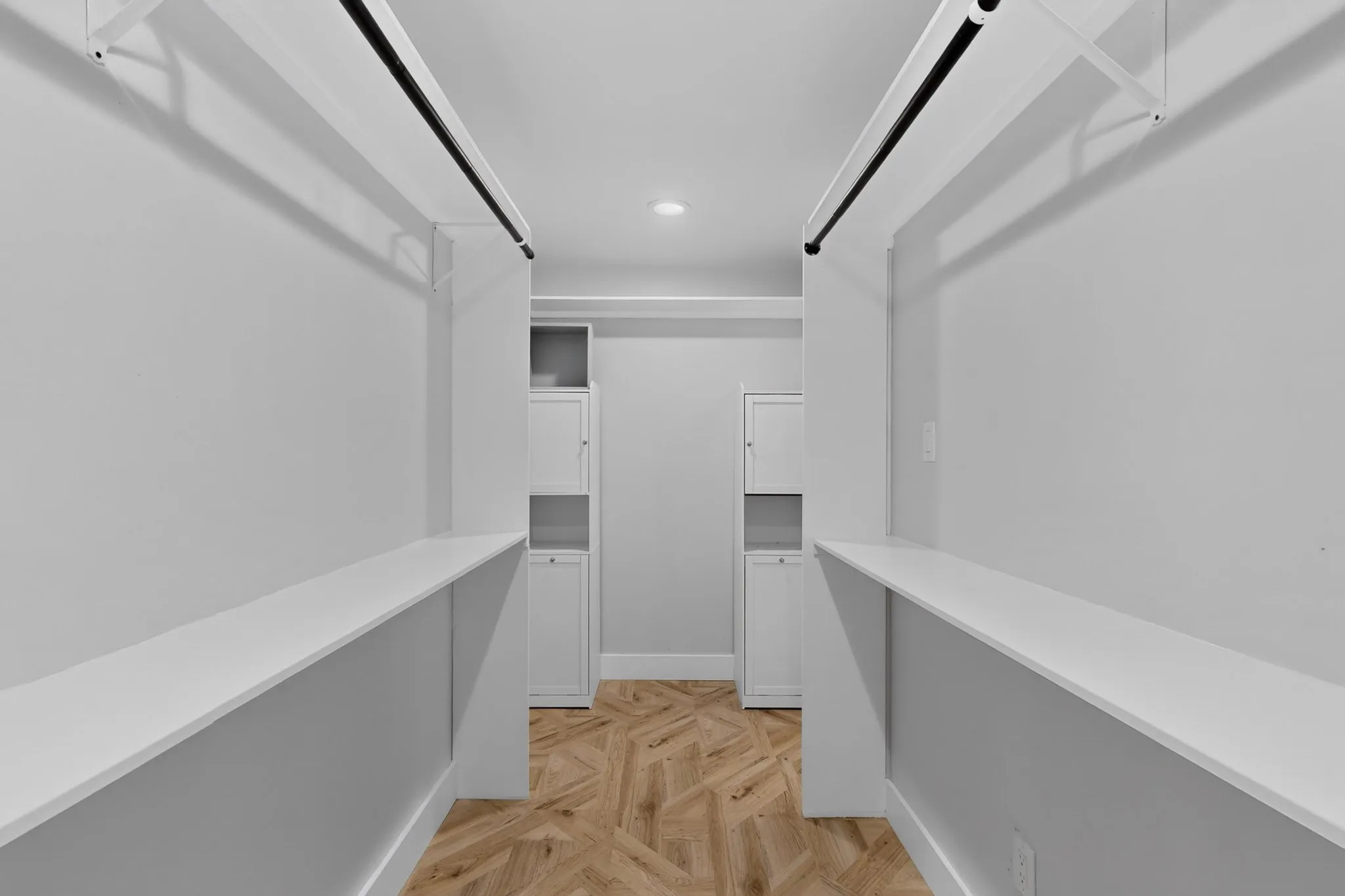 Walk-in closet featuring wood-finish flooring in a herringbone pattern, integrated shelving, and dedicated hanging rods