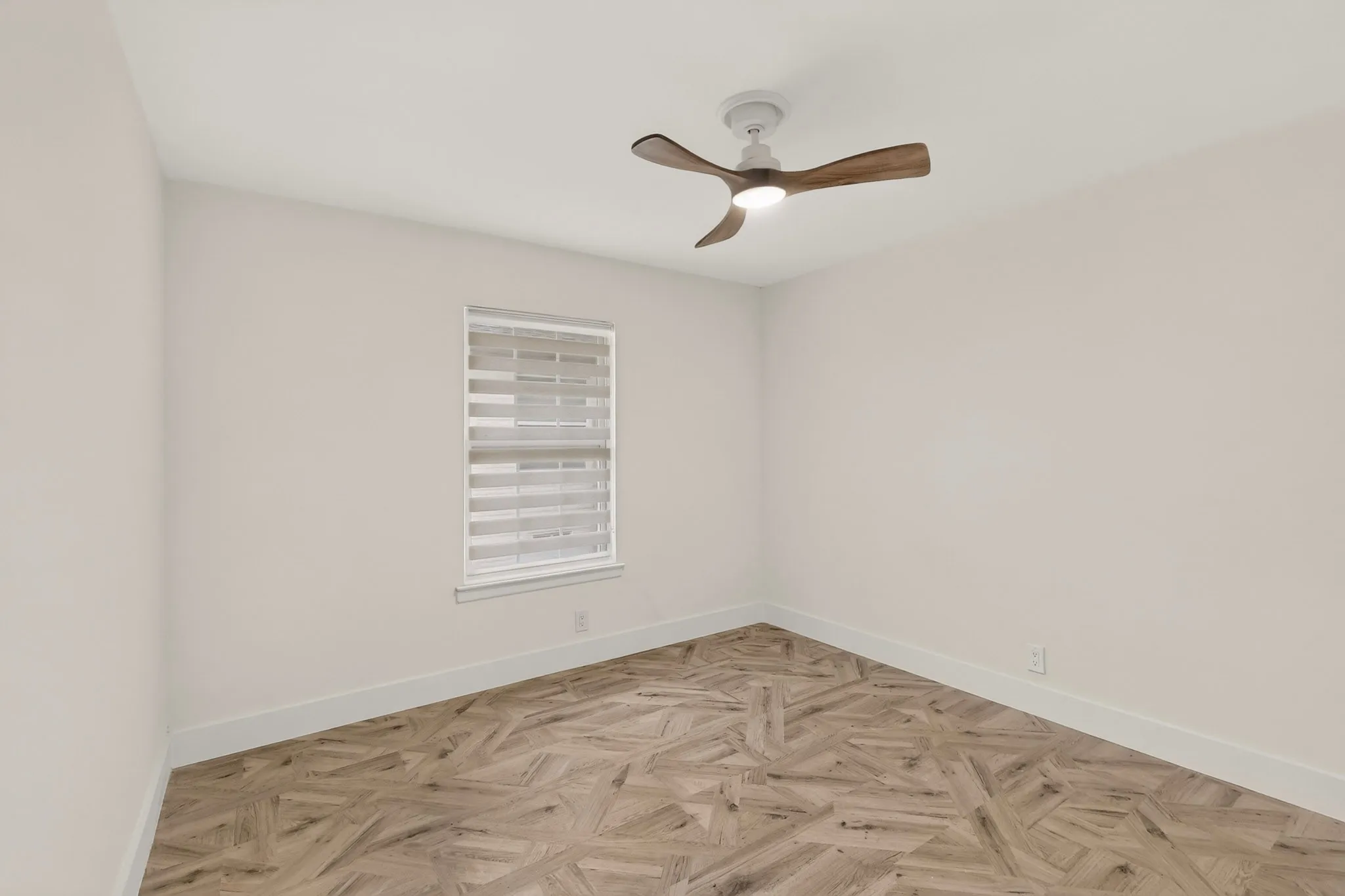 Well-lit room featuring light-toned walls, a white window frame with integrated blinds, and a contemporary ceiling fan with integrated lighting
