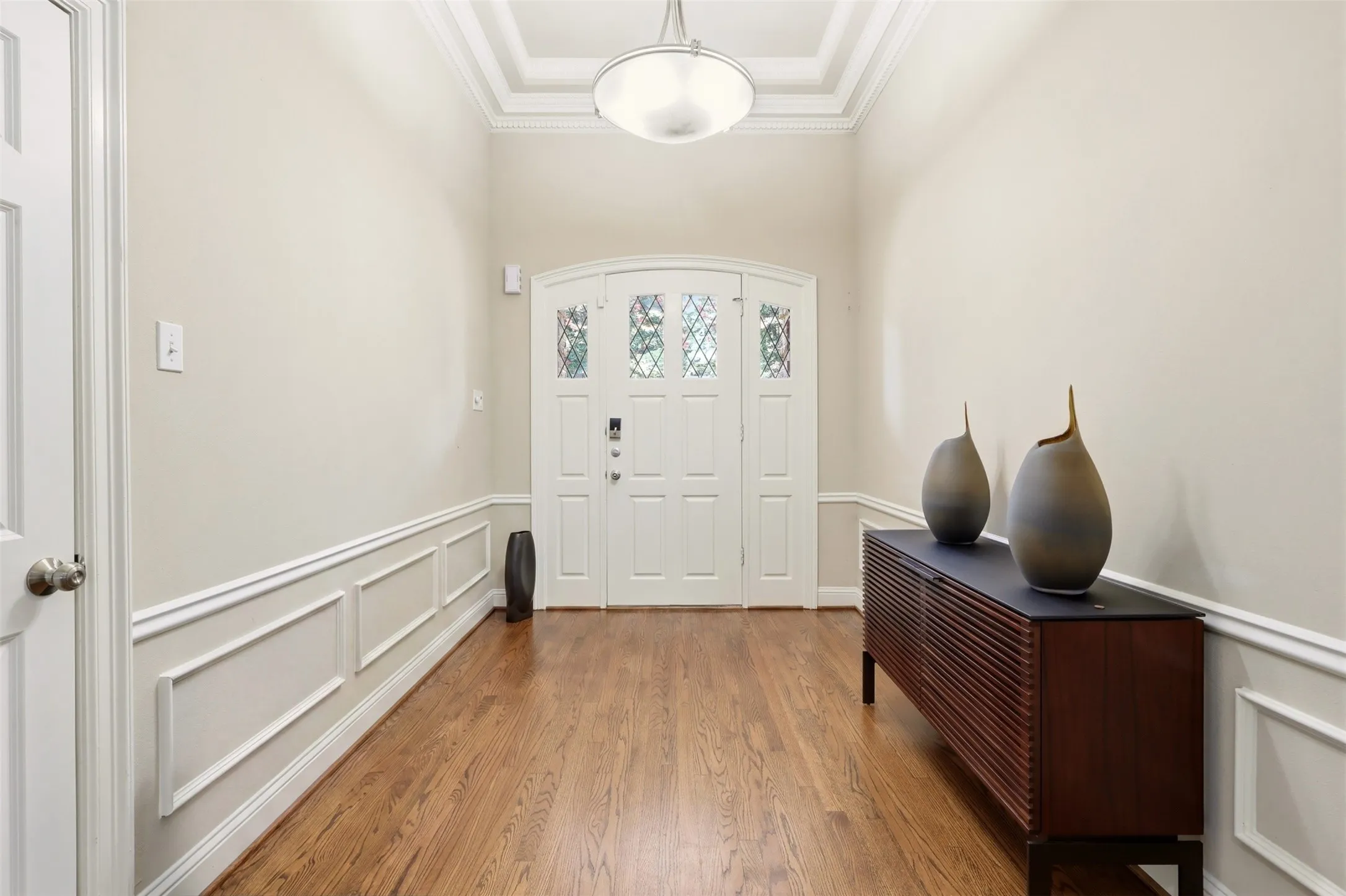 Entryway featuring wood-finish flooring, wainscoting, and a decorative arched double door with leaded glass panels