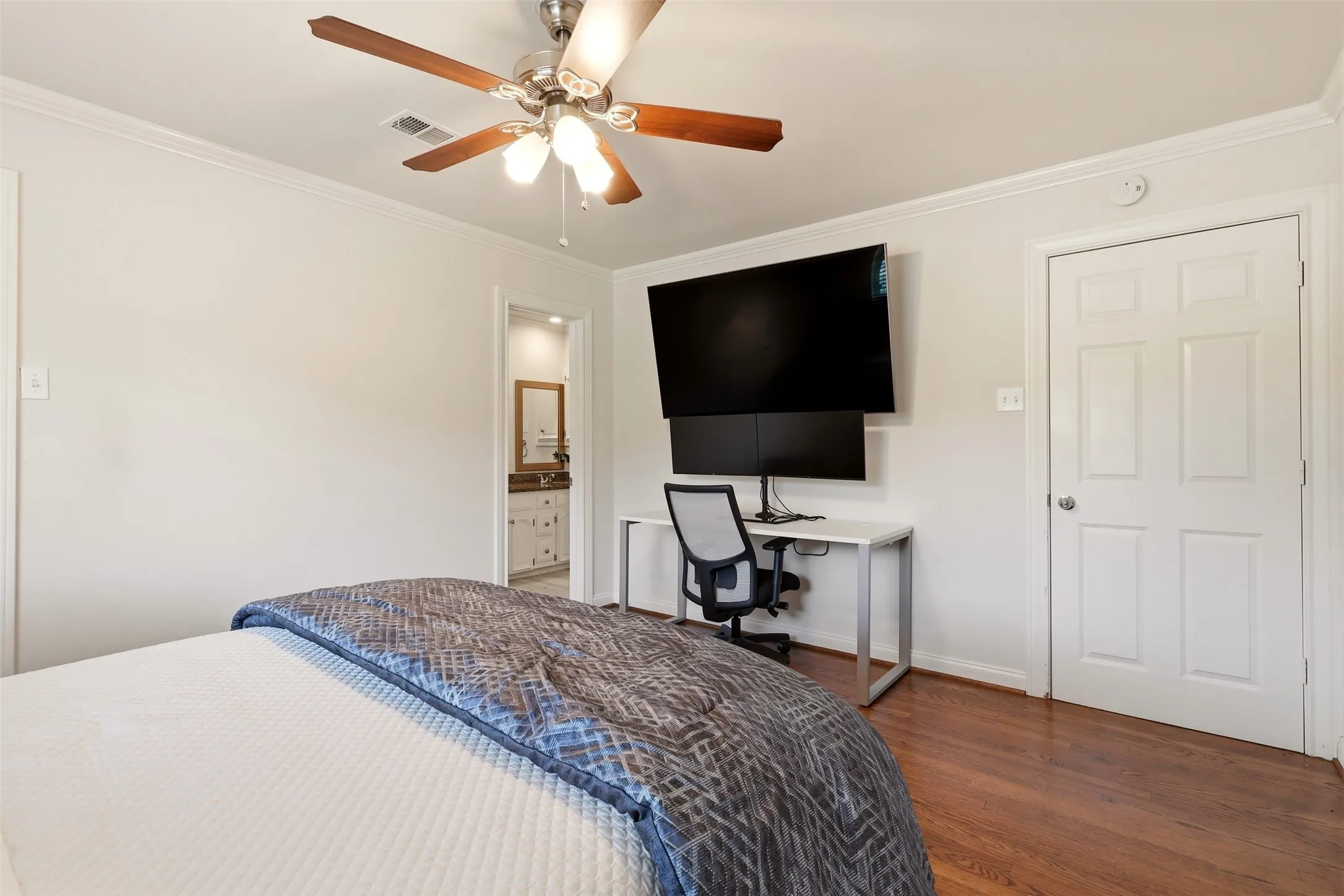 Bedroom featuring wood-finish flooring, a ceiling fan with light kit, crown molding, and a white paneled door