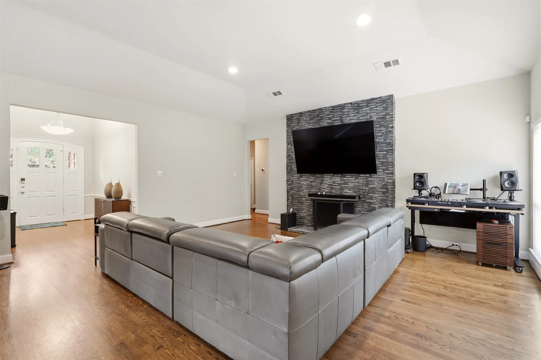 Spacious living area featuring wood-finish flooring, light-toned walls, and a stone-clad accent wall