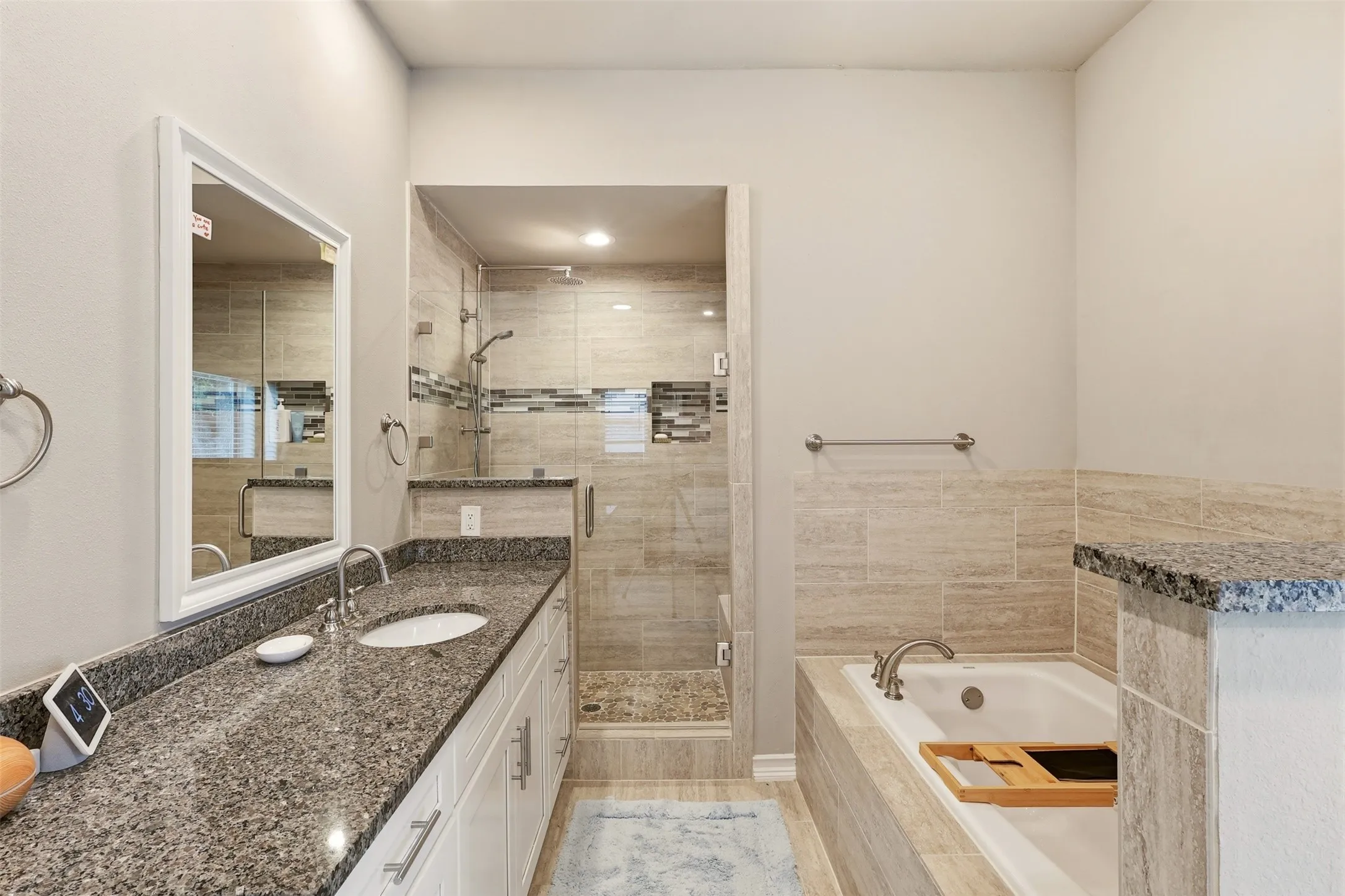 Bathroom featuring a full-size soaking tub, a walk-in shower with a glass enclosure, a vanity with a granite countertop, an undermount sink, and light-toned wall tile