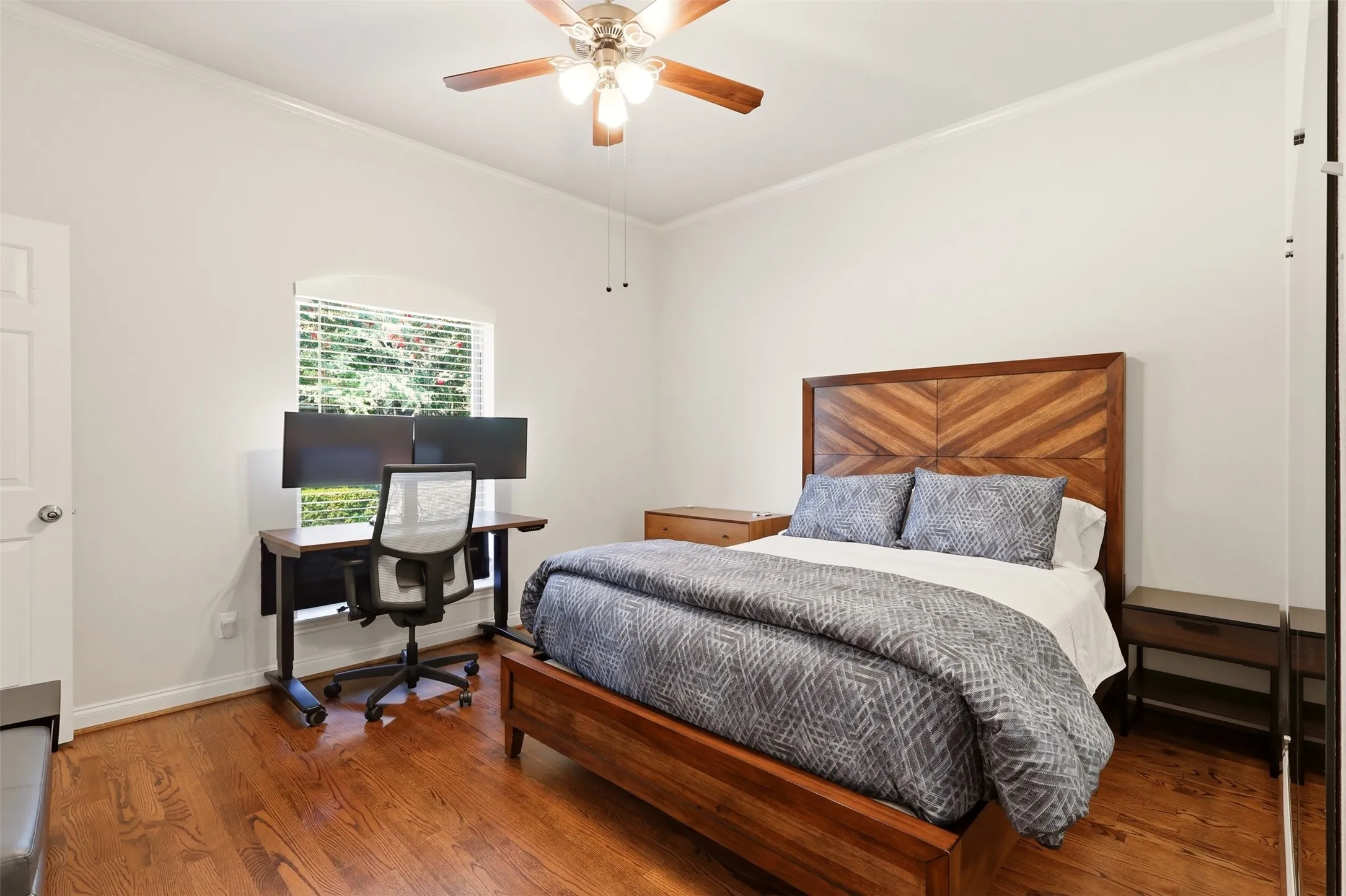 Bedroom featuring wood-finish flooring, a ceiling fan with integrated lighting, a window with horizontal blinds, and a white paneled door