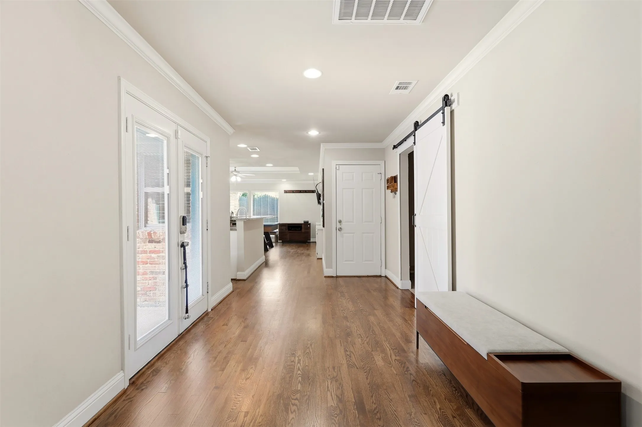 Hallway featuring wood-finish flooring, white French doors, recessed lighting, crown molding, and a white barn door