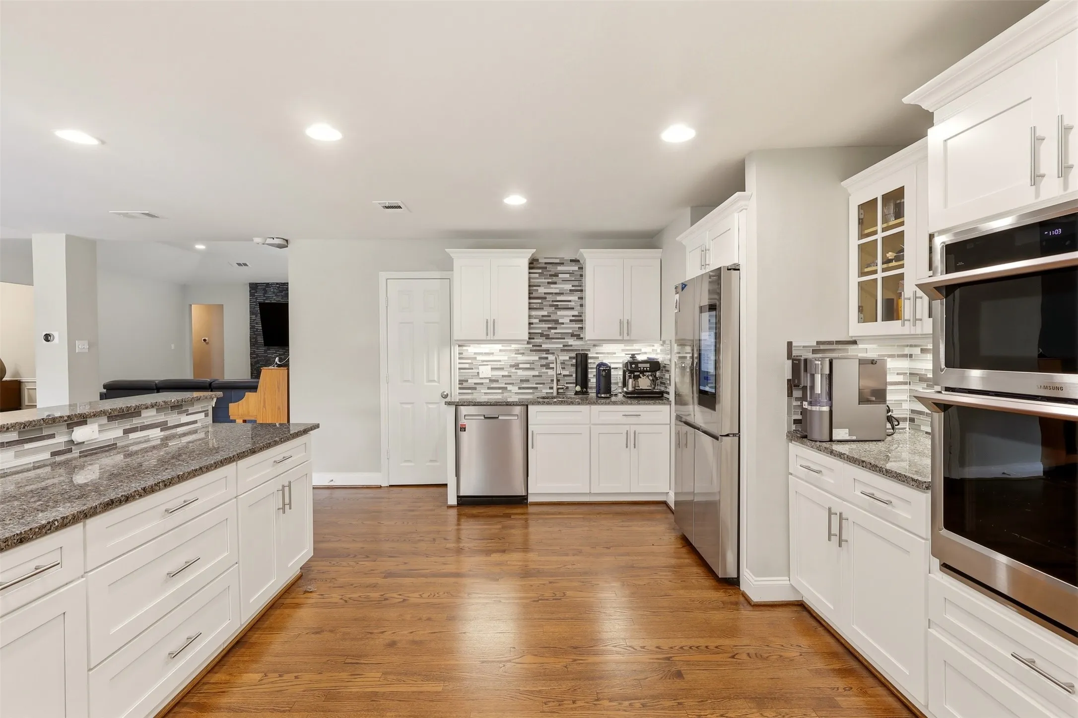 Kitchen featuring wood-finish flooring, white cabinetry, granite countertops, and stainless steel appliances including a built-in double oven, refrigerator, and dishwasher