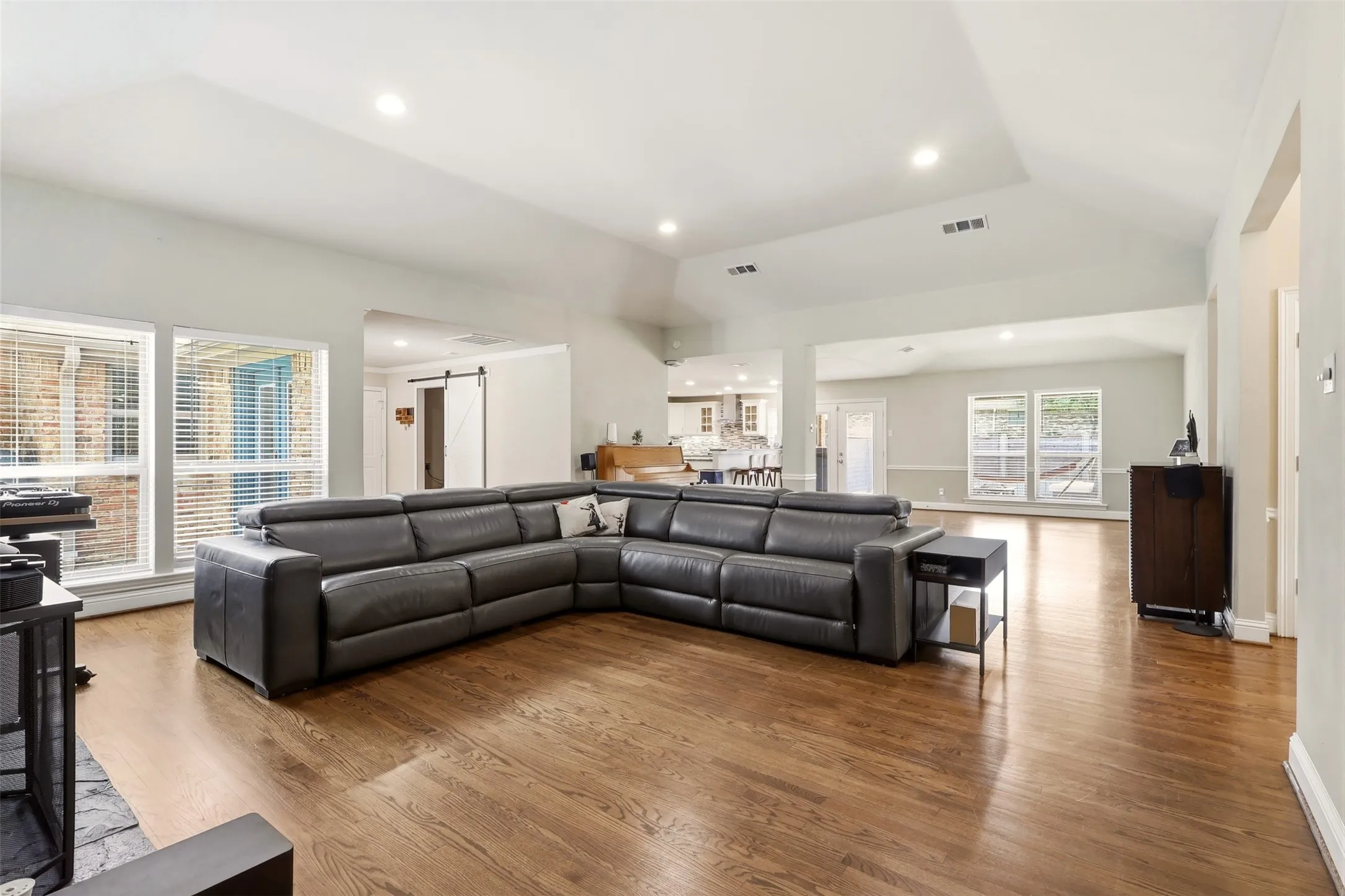 Spacious living area featuring vaulted ceilings, recessed lighting, hardwood flooring, and multiple large windows