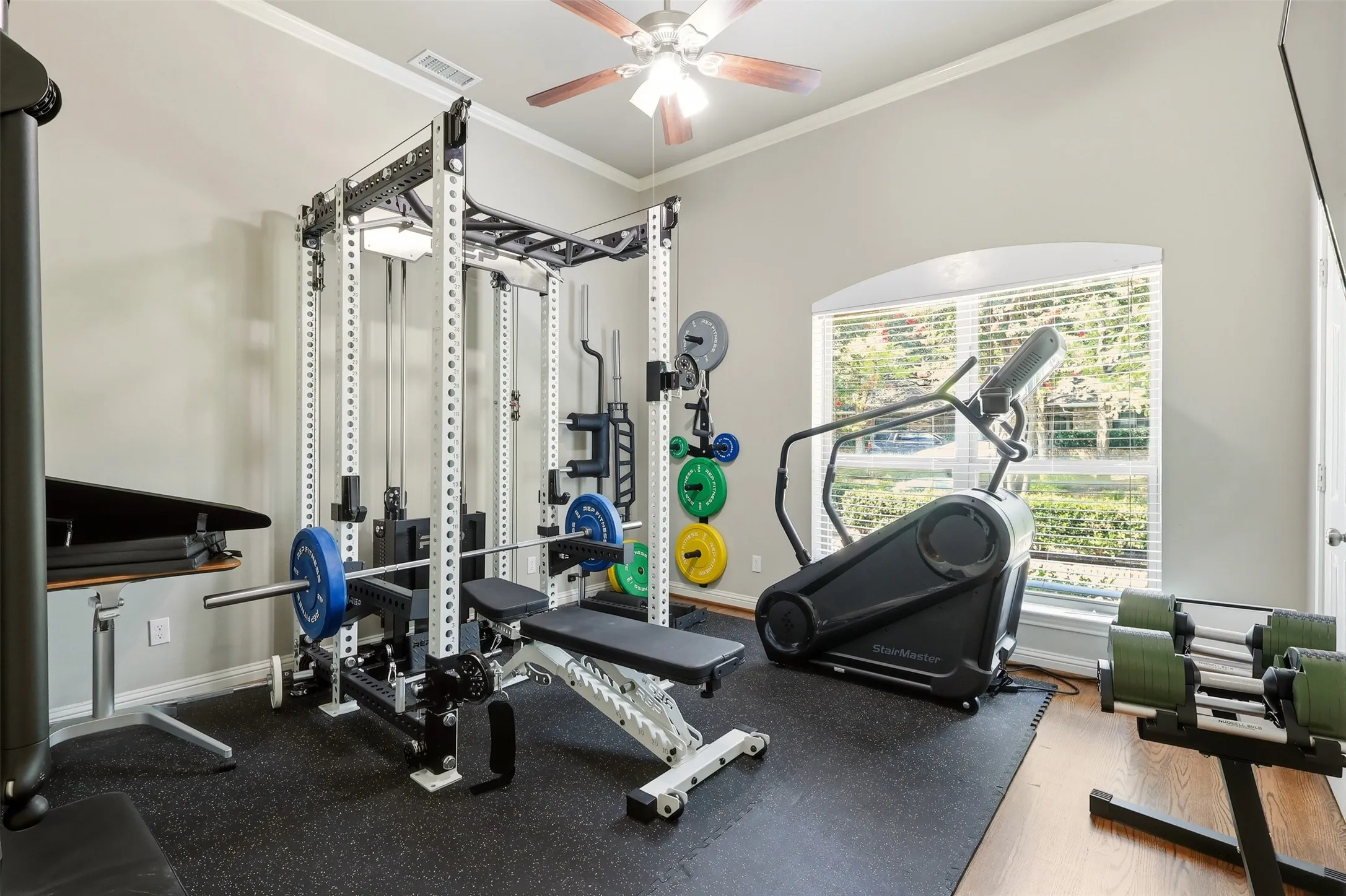 Dedicated exercise room featuring a vaulted ceiling with a ceiling fan, a large arched window with blinds, and durable rubber flooring