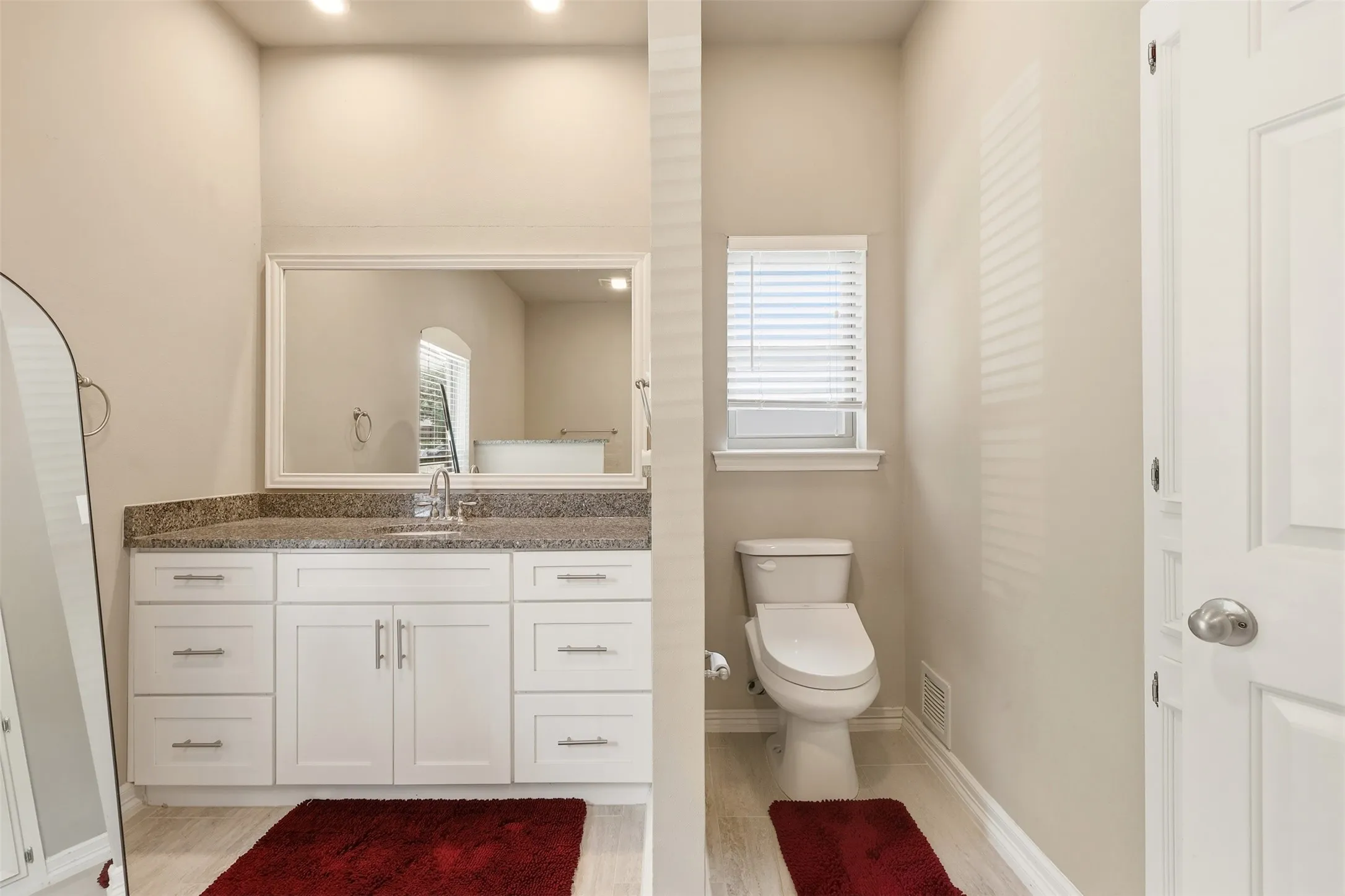 Bathroom featuring a white vanity with a stone countertop, a framed mirror, and a window with blinds