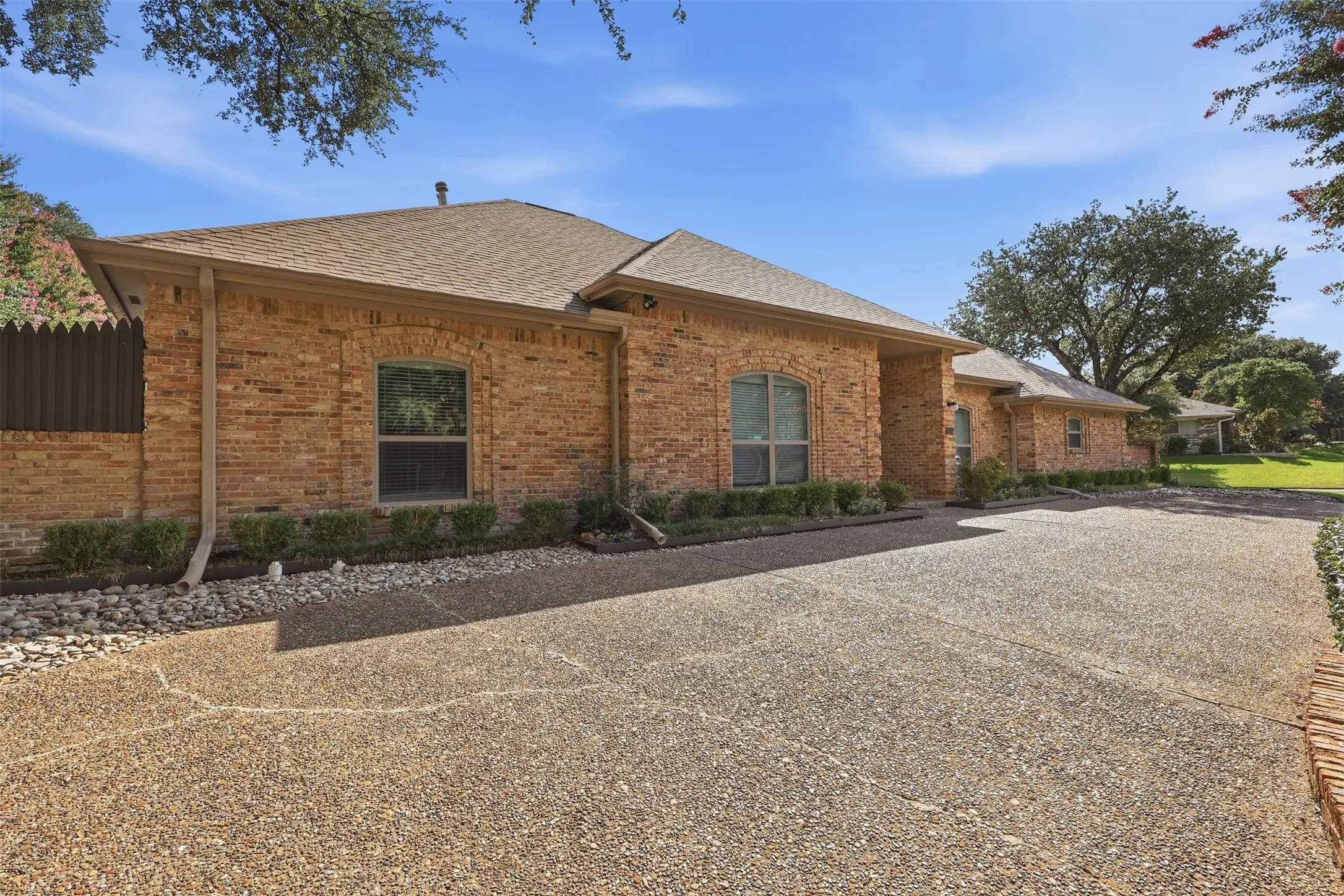 Brick exterior with arched windows, a textured driveway, and established landscaping
