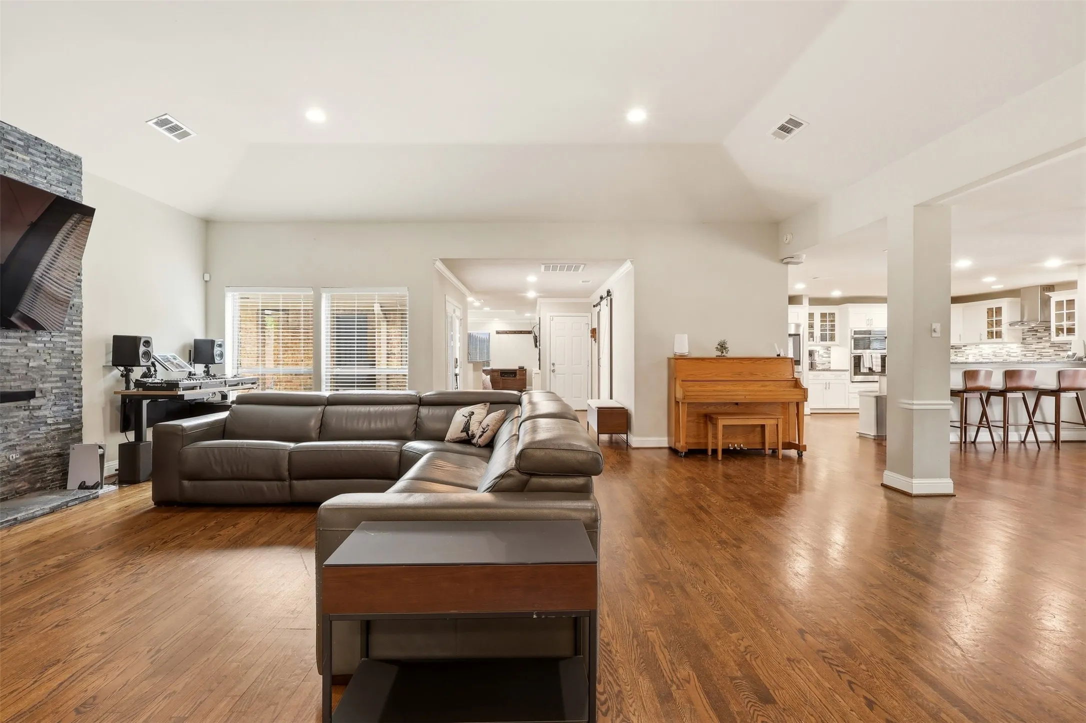 Spacious living area featuring wood-finish flooring, a stone-clad fireplace, recessed lighting, and vaulted ceilings