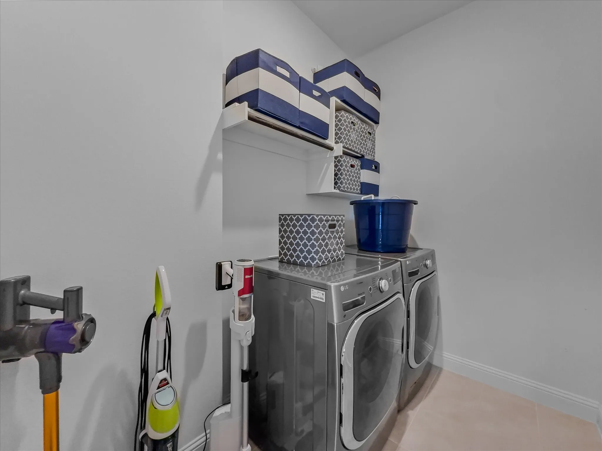 Dedicated laundry area with front-load washer and dryer, complemented by white wall-mounted shelving and light-toned flooring