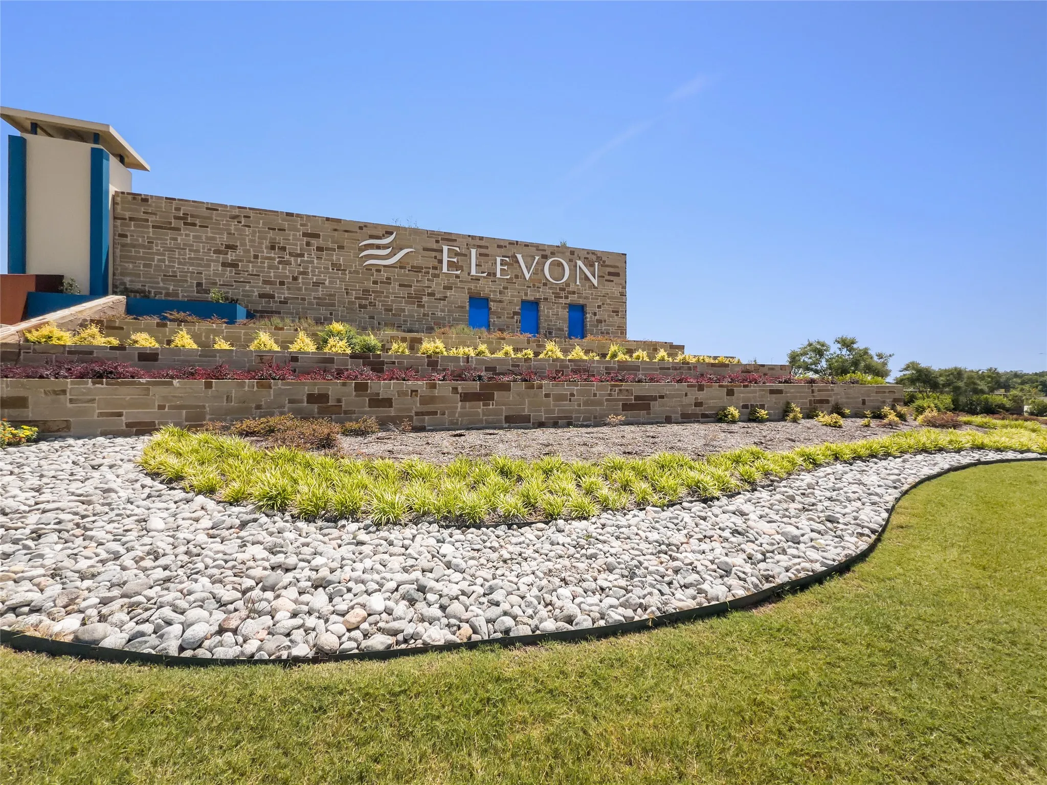 Stone-clad architectural element featuring a prominent sign, tiered landscaping, and vibrant plantings