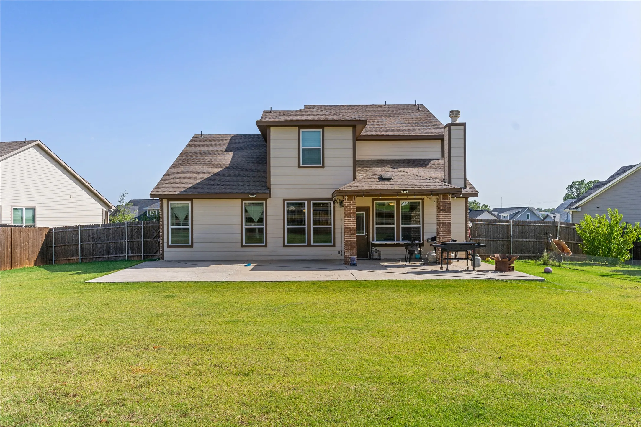 Expansive backyard featuring a large concrete patio, a blend of brick and siding exterior, a wood fence boundary, and multiple windows across the rear facade