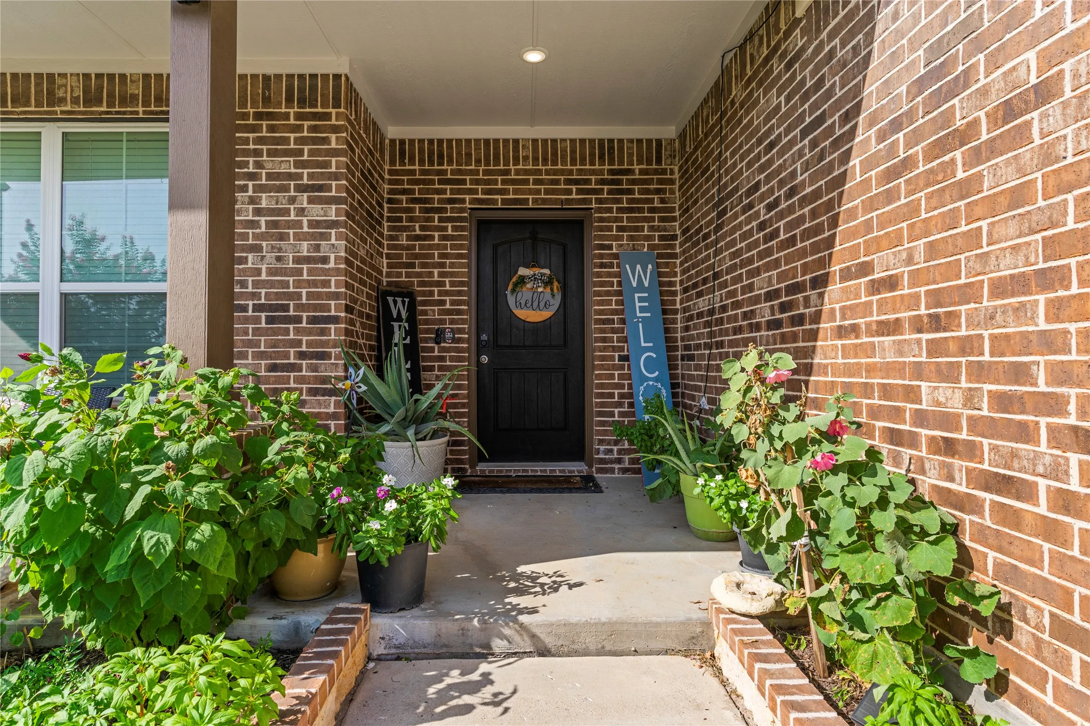 Front entry featuring a paneled black door, brick facade, recessed lighting, and a covered porch