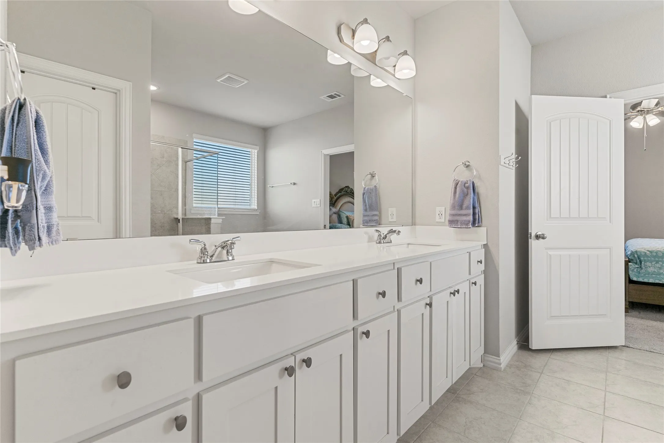 Dual vanity featuring white cabinetry, integrated sinks, chrome faucets, and a large mirror with overhead lighting