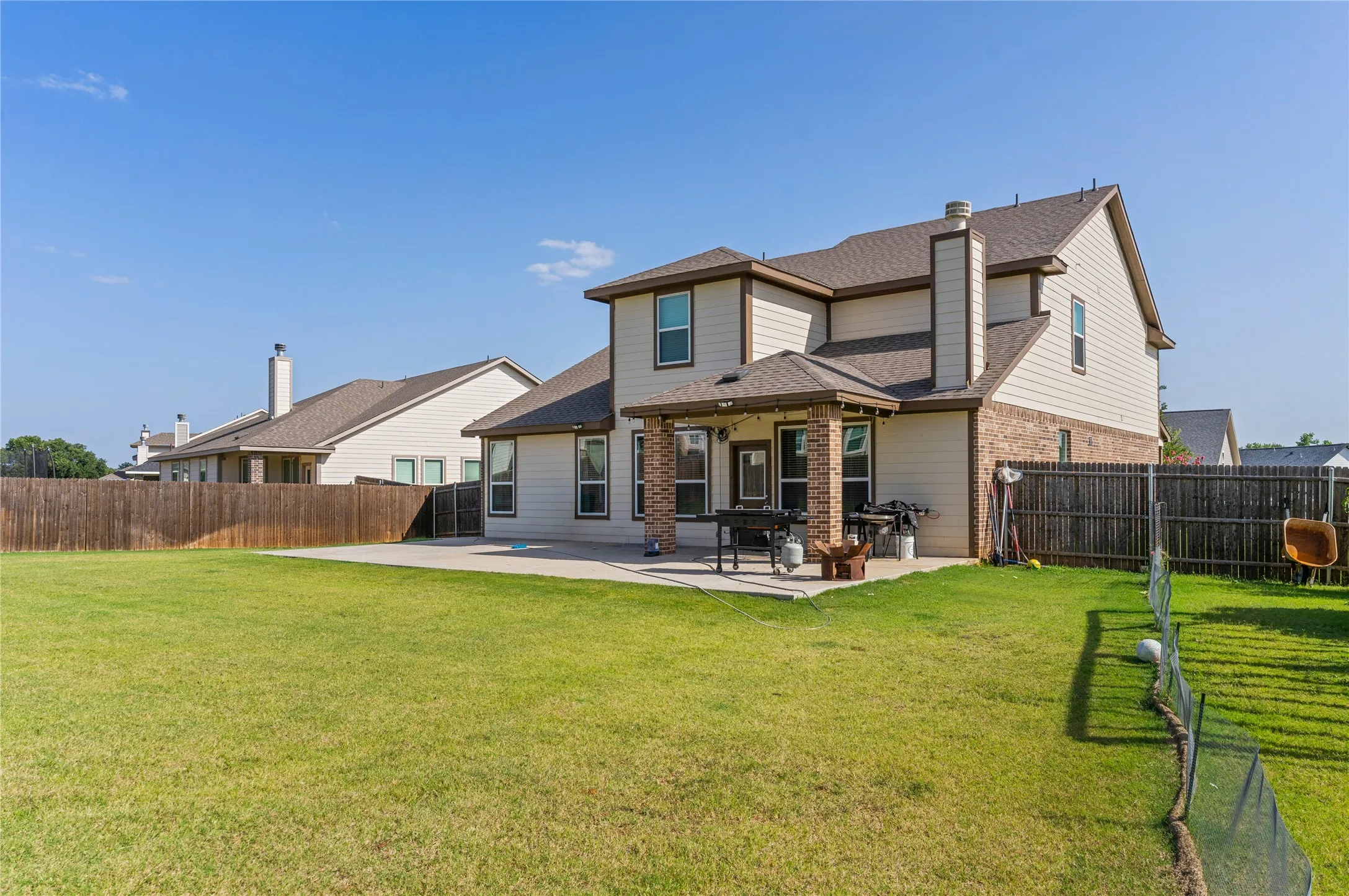 Spacious backyard featuring a large concrete patio, privacy fencing, and a two-story residence with brick and siding exterior