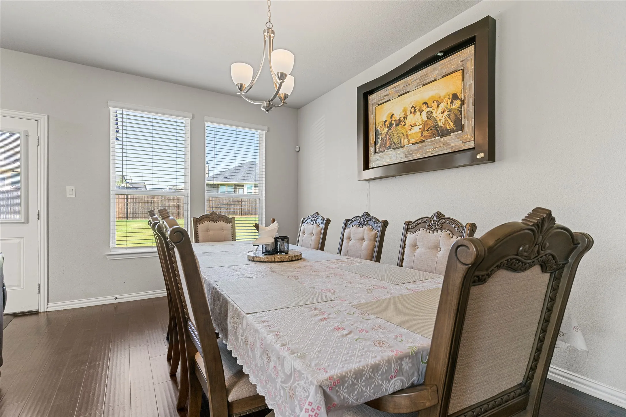 Dining area featuring dark wood-finish flooring, light grey wall paint, and a traditional chandelier with frosted glass shades