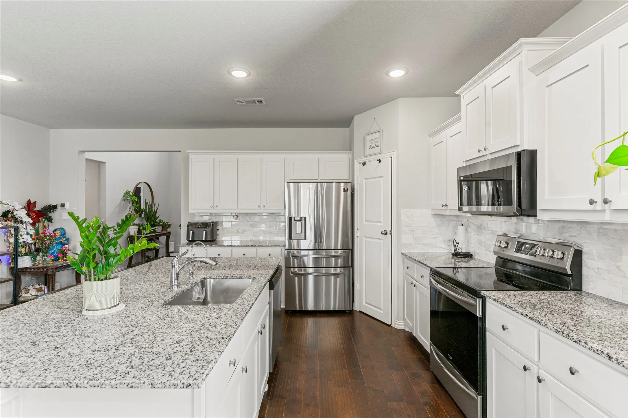 Bright kitchen featuring a large central island with an undermount sink, stainless steel appliances, white cabinetry, granite countertops, and wood-finish flooring