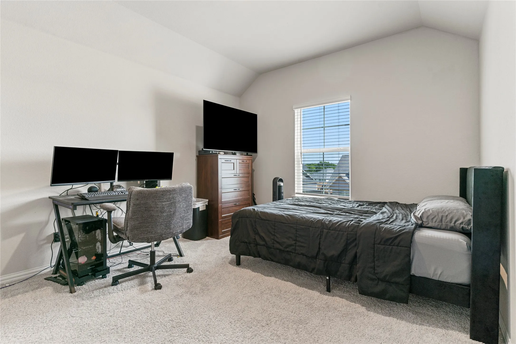 Carpeted bedroom with a vaulted ceiling and a single window featuring blinds