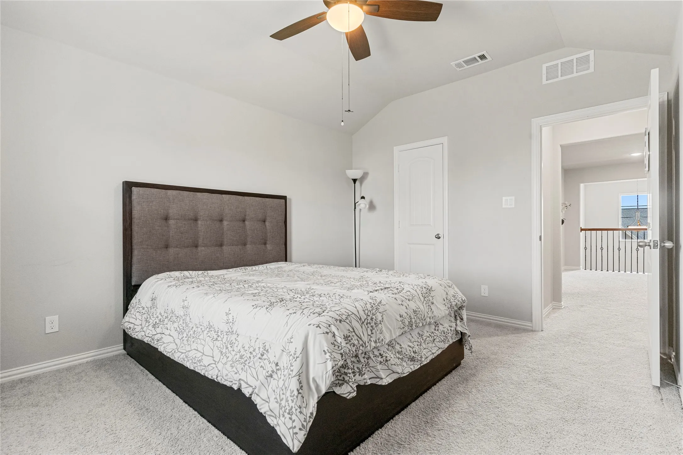 Vaulted ceiling bedroom featuring plush light-toned carpeting, a ceiling fan with light fixture, and white trim
