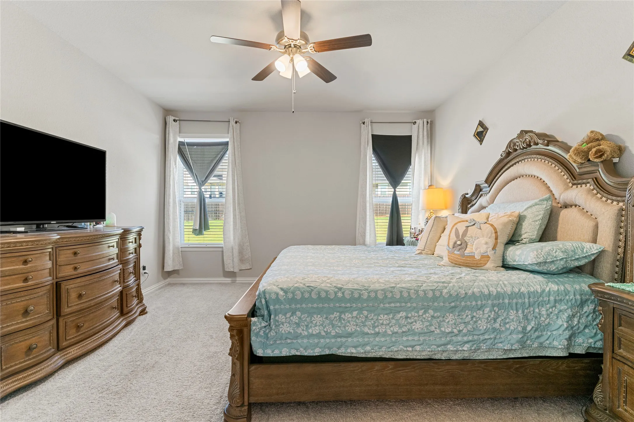 Carpeted bedroom featuring two windows with blinds and curtains, a ceiling fan with integrated lighting, and neutral wall tones
