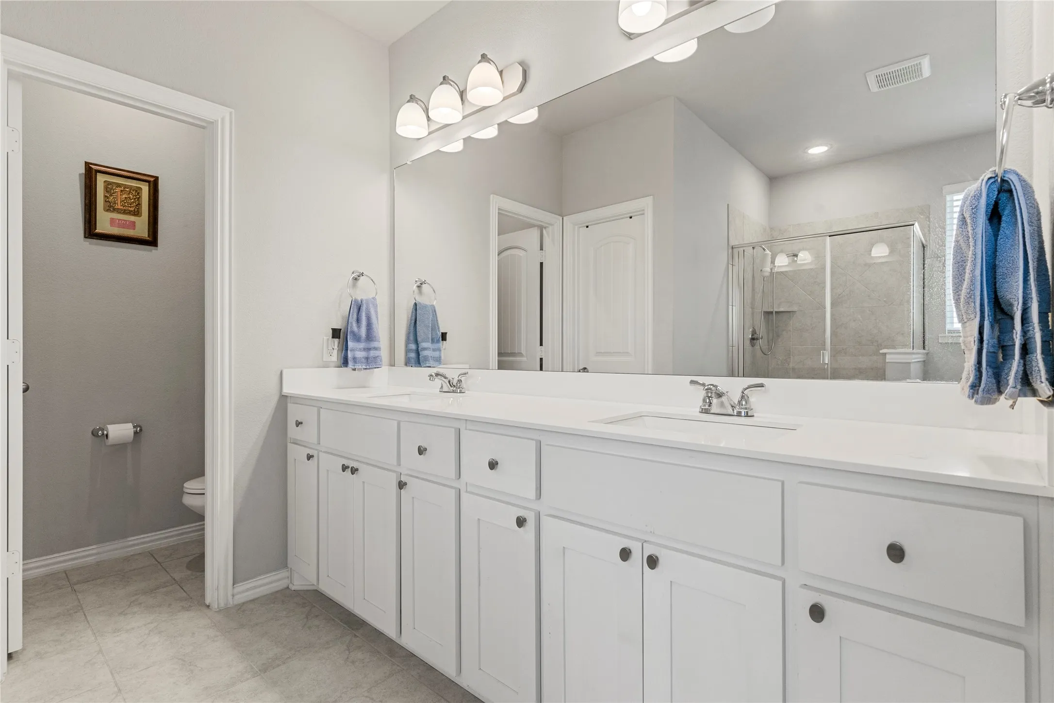 Dual vanity with white cabinetry and integrated sinks, illuminated by a multi-bulb light fixture