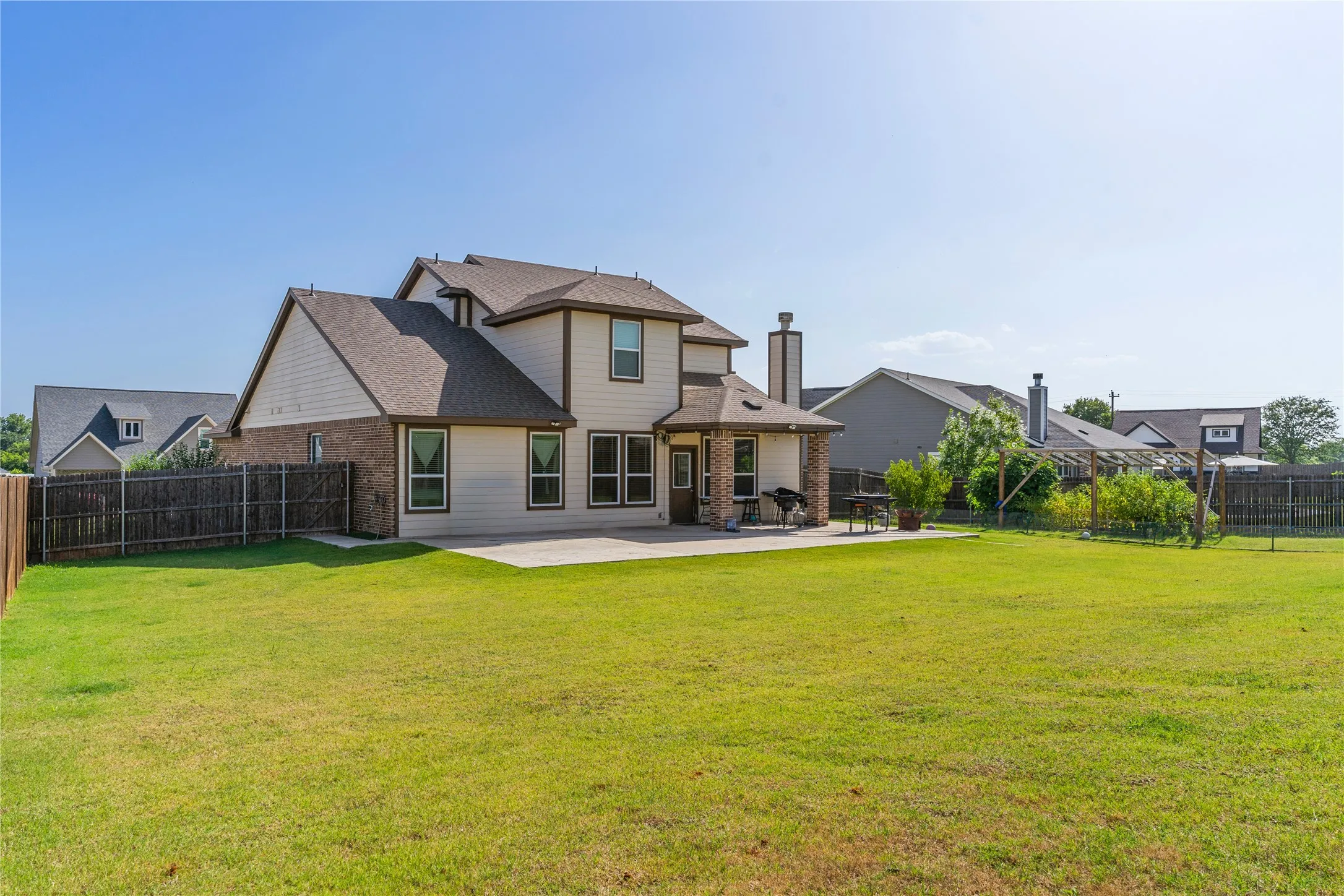 Expansive backyard featuring a large concrete patio, a pergola structure, and a full privacy fence