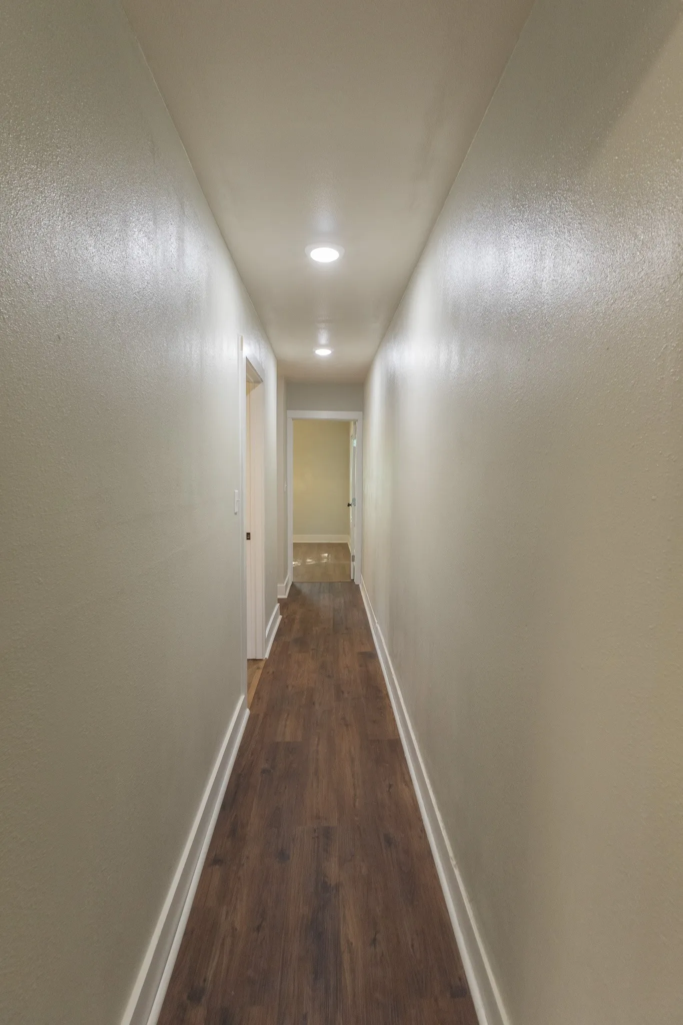 Hallway featuring recessed lighting, wood-finish flooring, light neutral wall color, white trim, and a white interior door