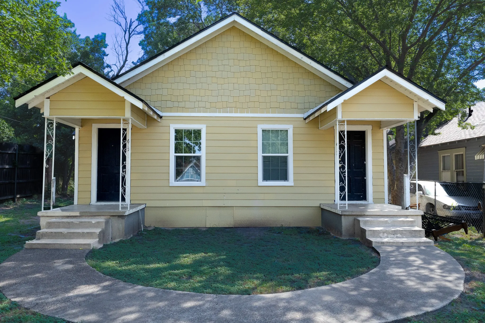 Duplex exterior featuring light yellow siding and a shingle-style gable accent