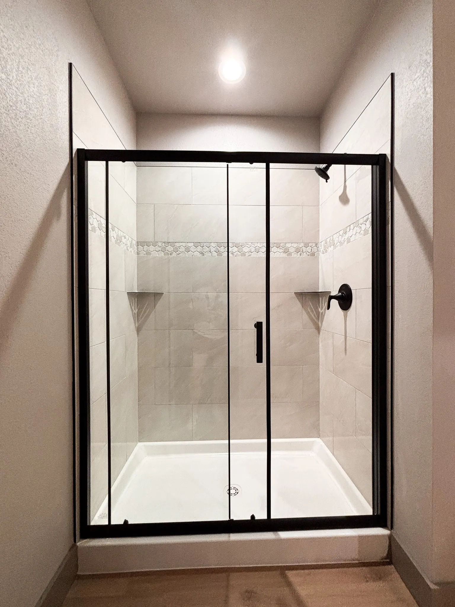 Enclosed shower with a black-framed glass door, featuring neutral-toned tile walls with a decorative accent band