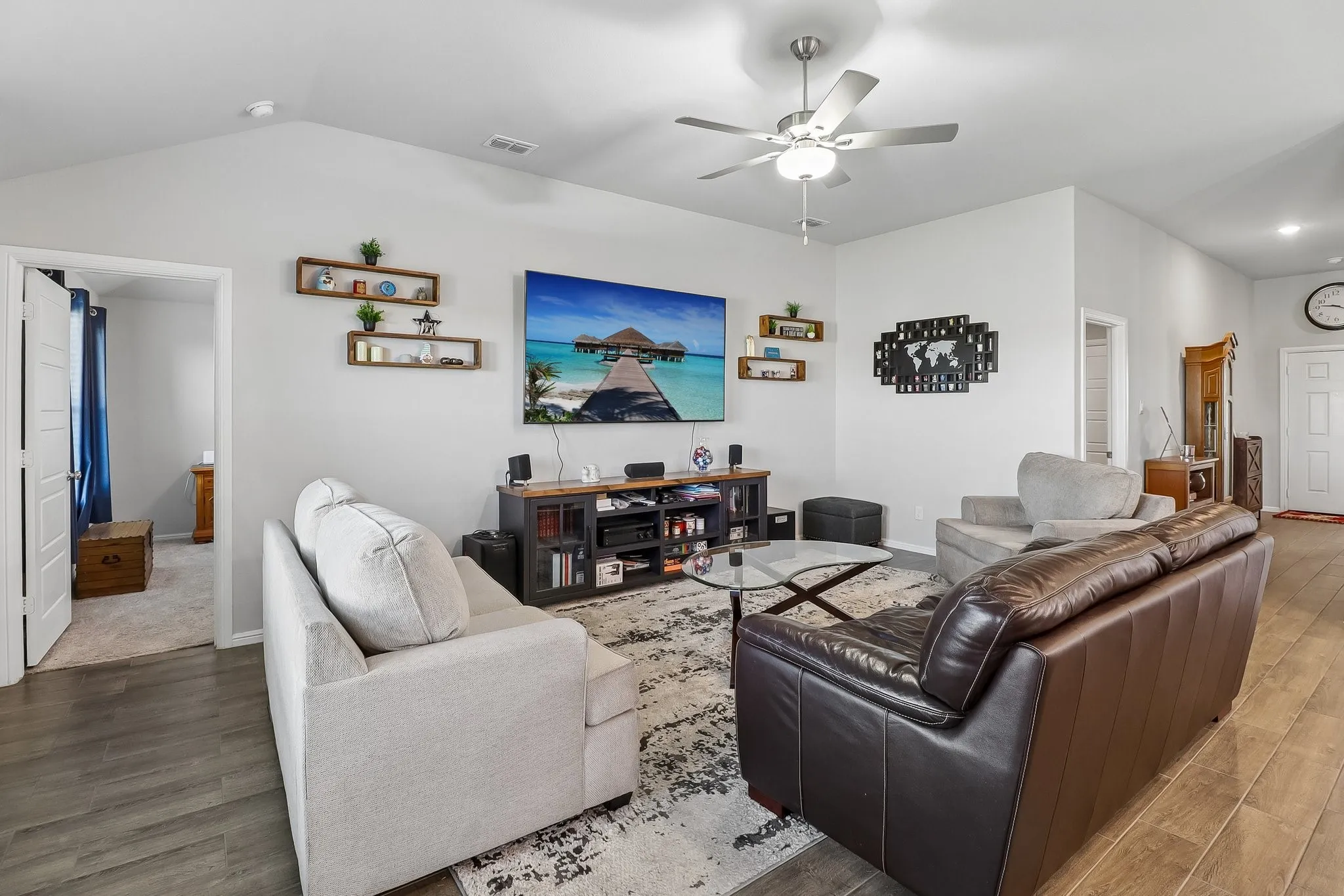 Living area featuring vaulted ceilings, wood-finish flooring, a ceiling fan with integrated lighting, and a white paneled door