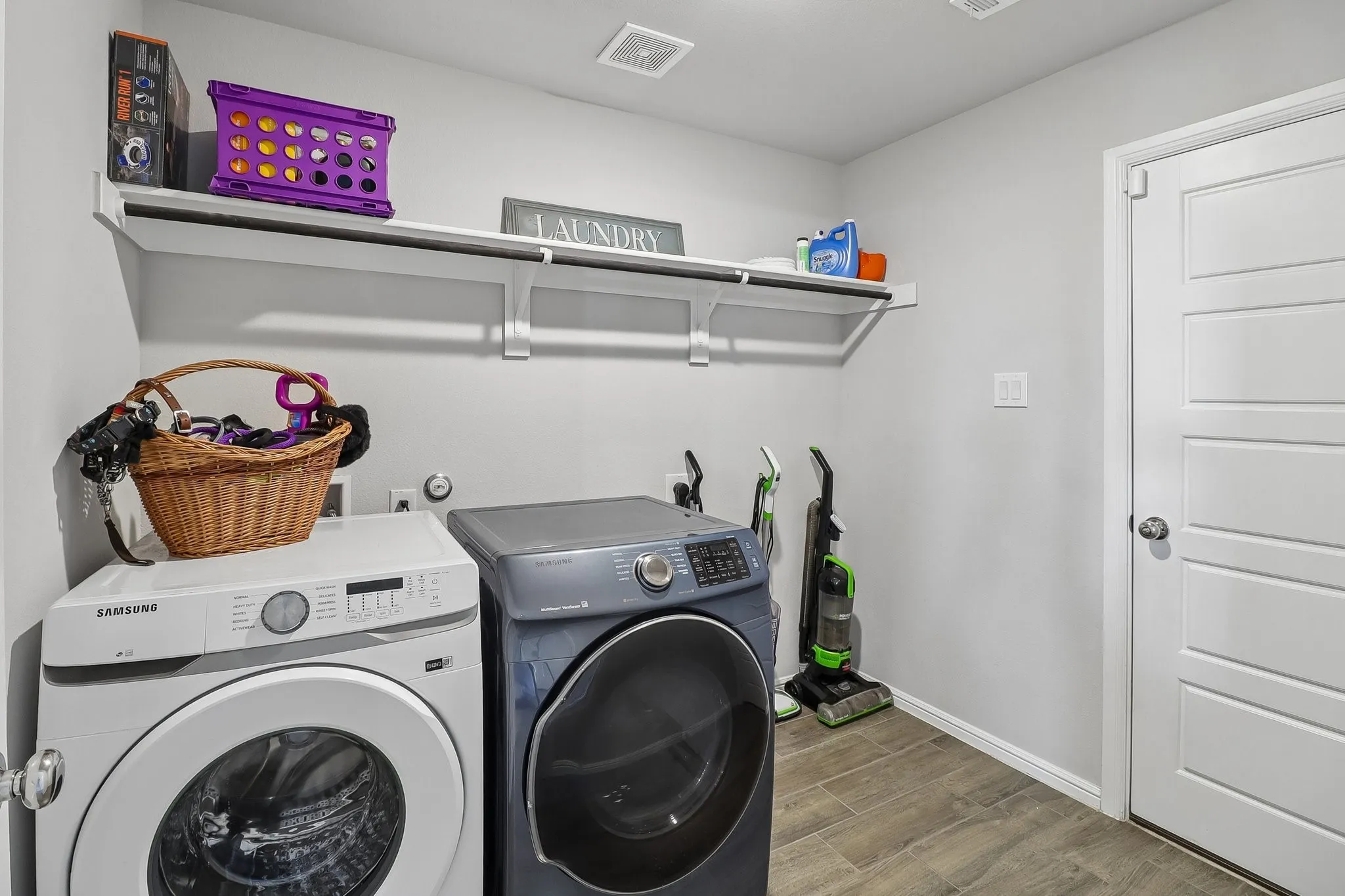Dedicated laundry area featuring modern front-loading appliances, wood-finish tile flooring, integrated shelving, and a hanging rod