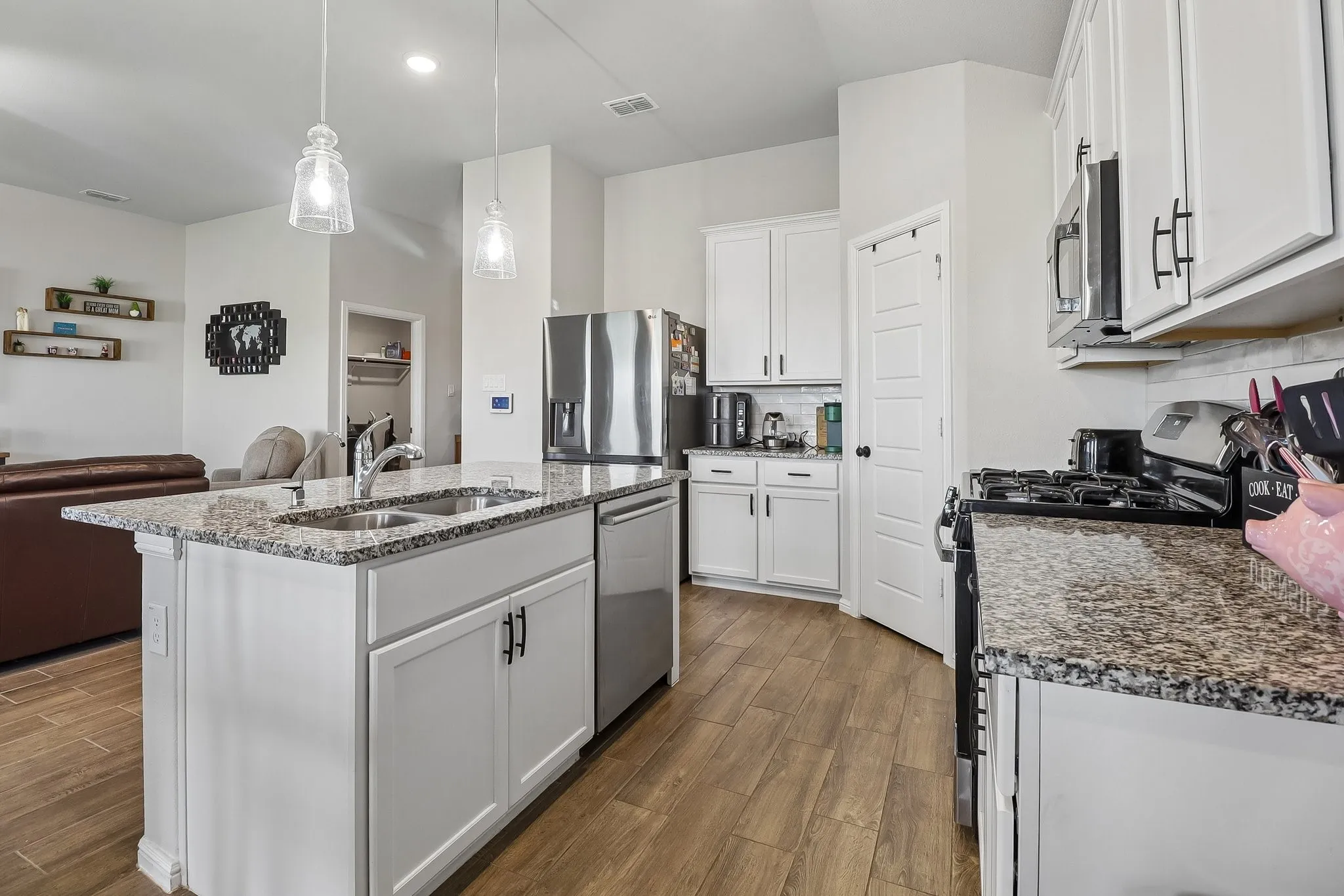 Kitchen featuring an island with granite countertops, stainless steel appliances, white cabinetry, and wood-finish flooring