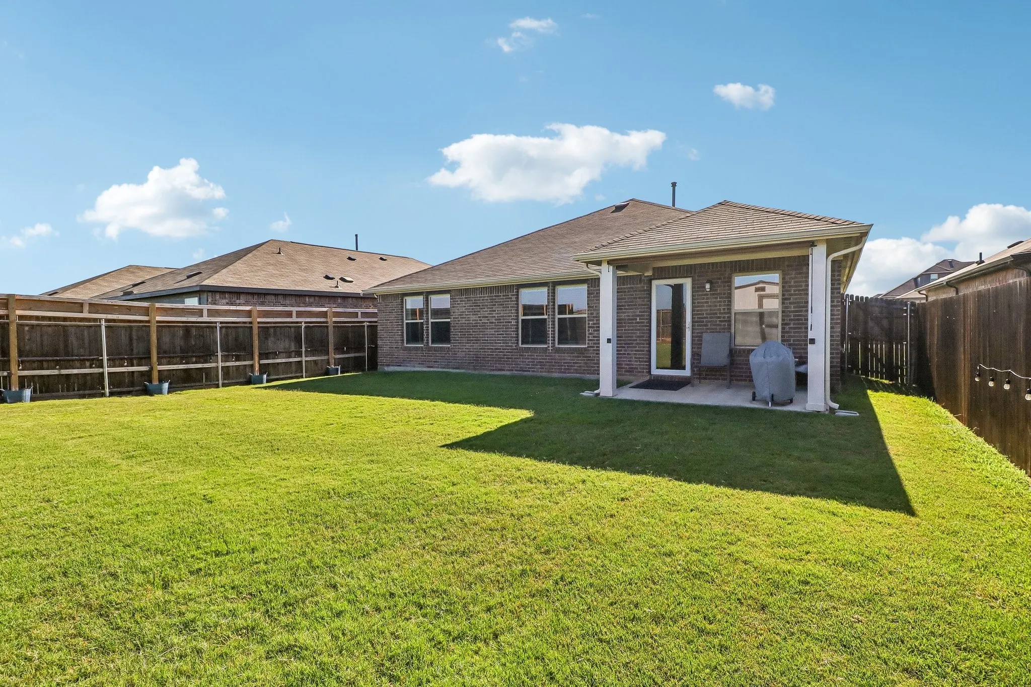 Expansive backyard featuring a manicured lawn, full privacy fencing, and a covered concrete patio