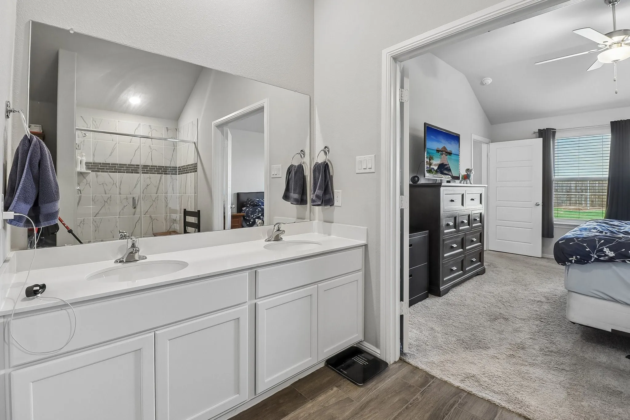 Dual vanity featuring white cabinetry and integrated sinks, a large wall-mounted mirror, and wood-finish flooring