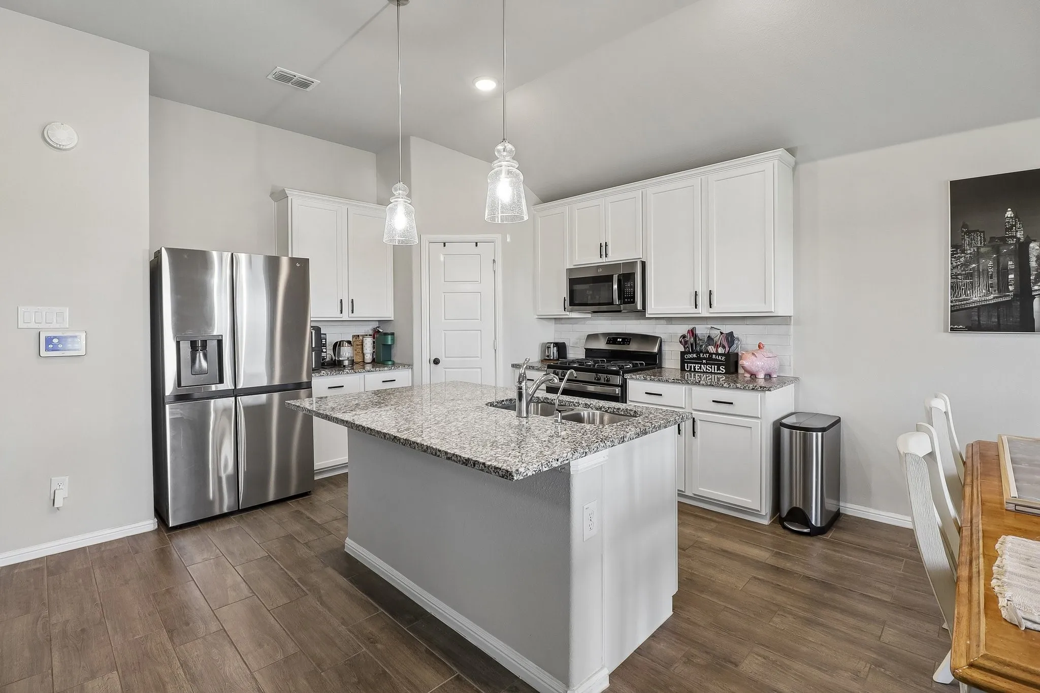 Open-concept kitchen featuring an island with a double basin sink, granite countertops, wood-finish flooring, white cabinetry, and stainless steel appliances